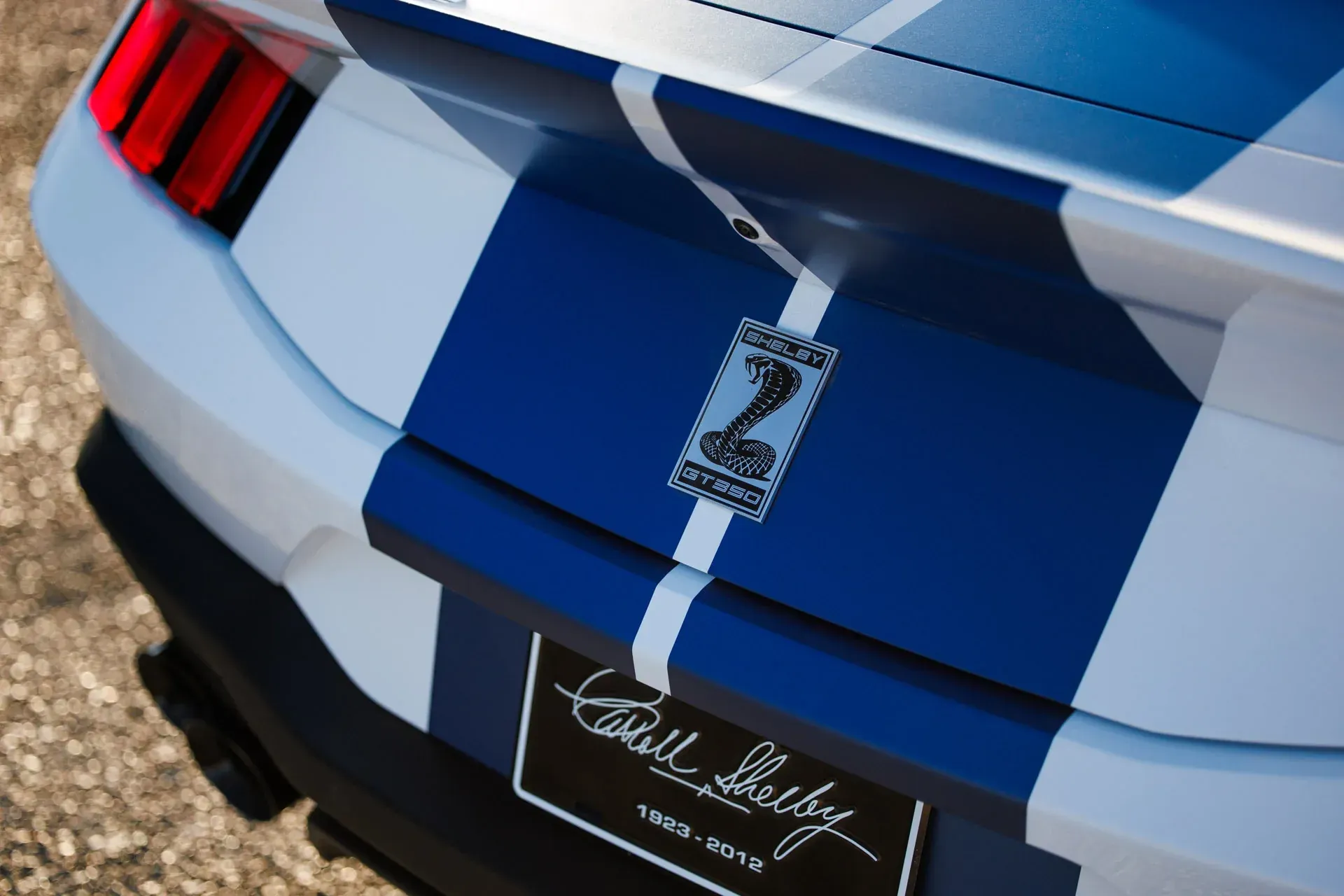Rear view of a blue and white Ford Mustang with racing stripes and Shelby Cobra emblem