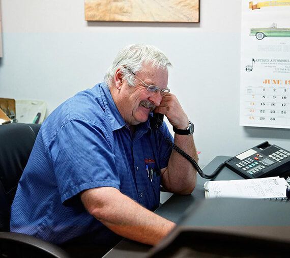 Man in blue shirt smiling while talking on a desk phone in an office