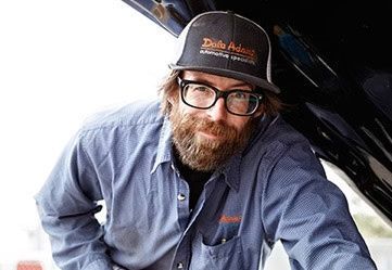 Smiling mechanic wearing glasses and a cap, holding a can | Dale Adams Automotive Specialists