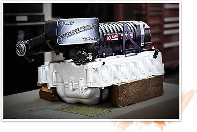 Supercharger on a white engine block sitting on wooden blocks