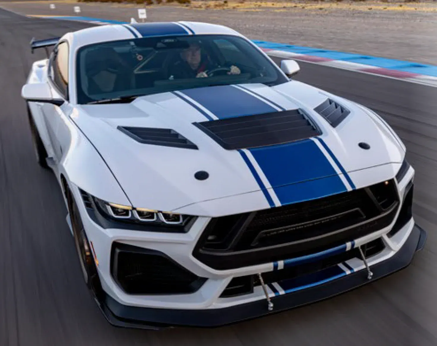 White sports car with blue racing stripes driving on a track, front view