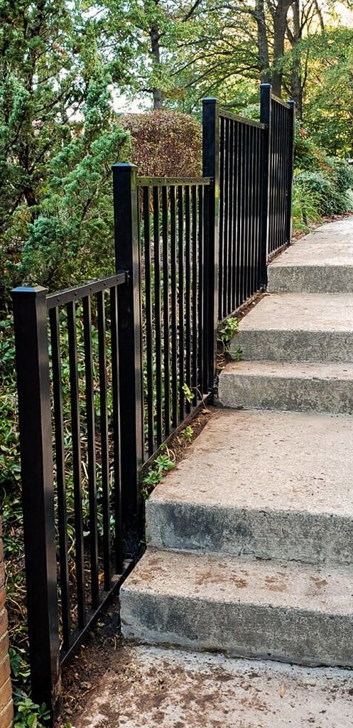 Black railing beside a set of outdoor concrete stairs, with trees in the background.