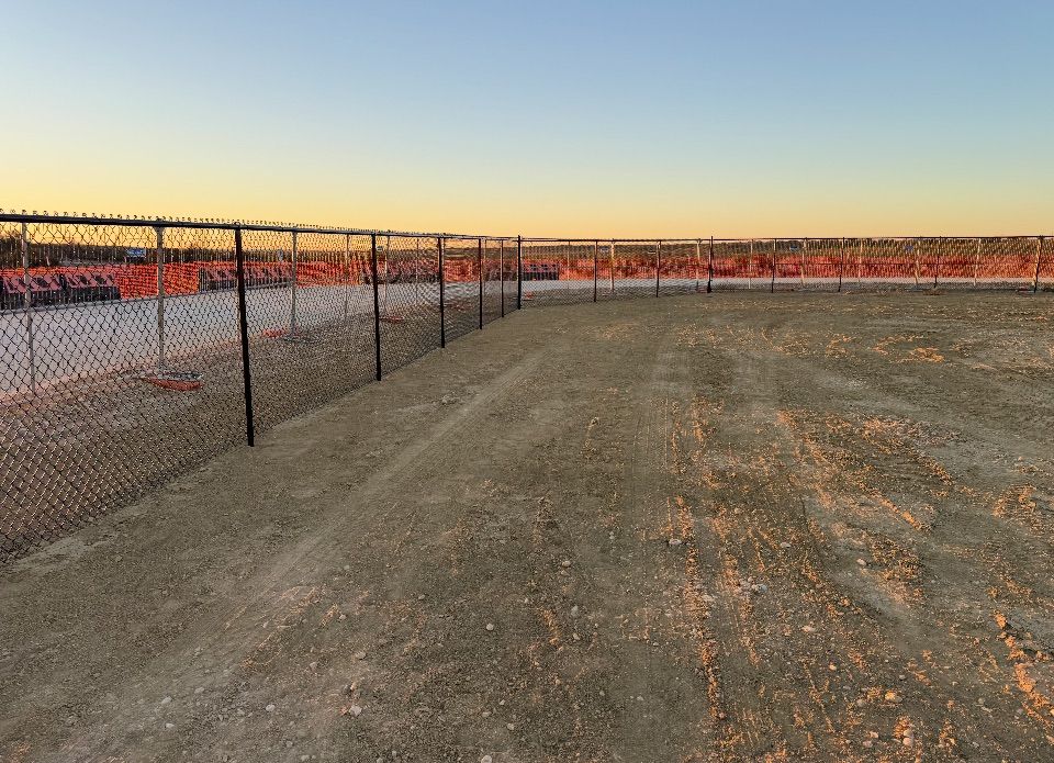 Chain-link fence in an empty dirt lot at dusk, with red construction visible in the background.