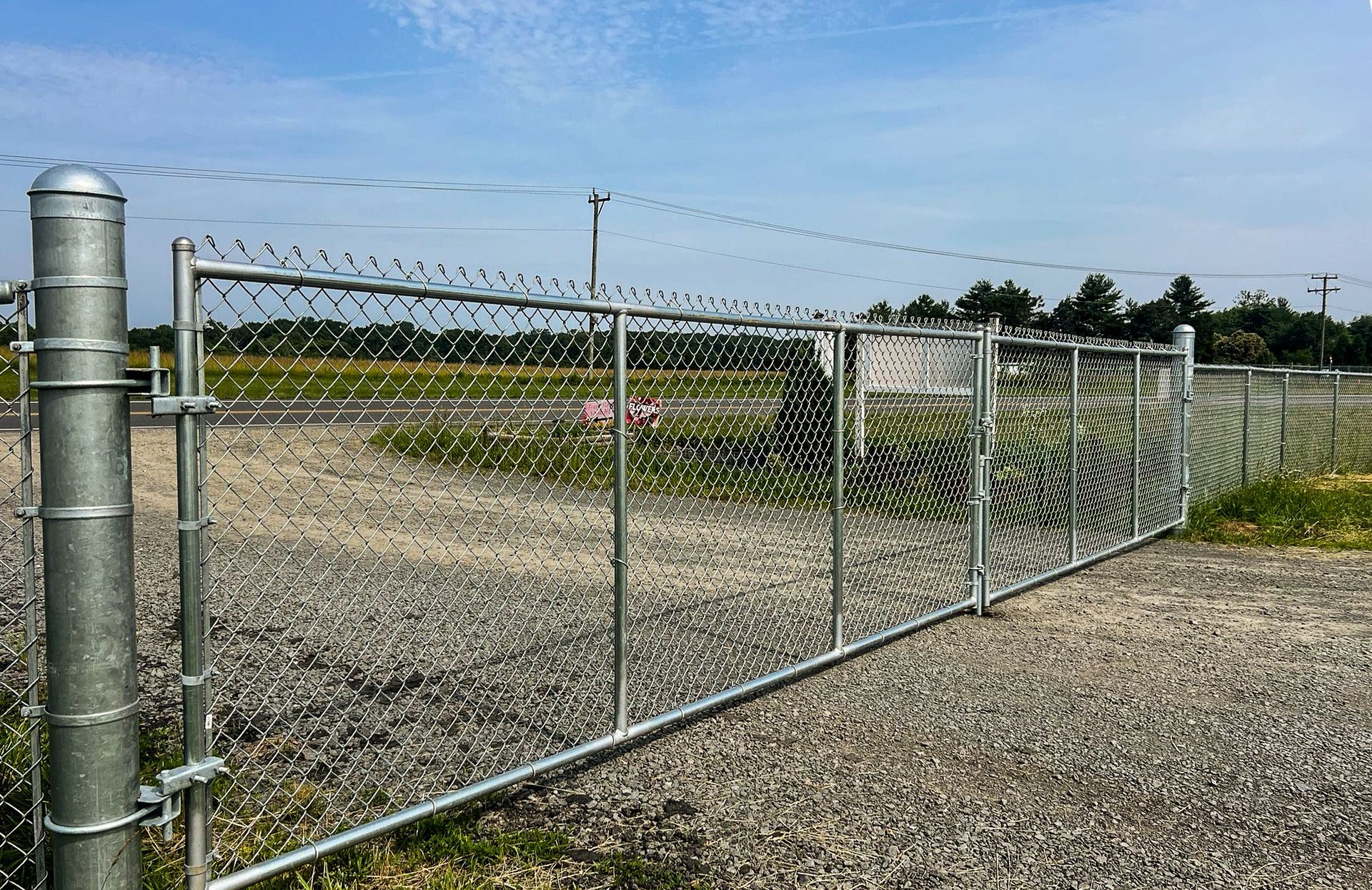Chain-link fence with gate, surrounding a gravel area, under a blue sky.