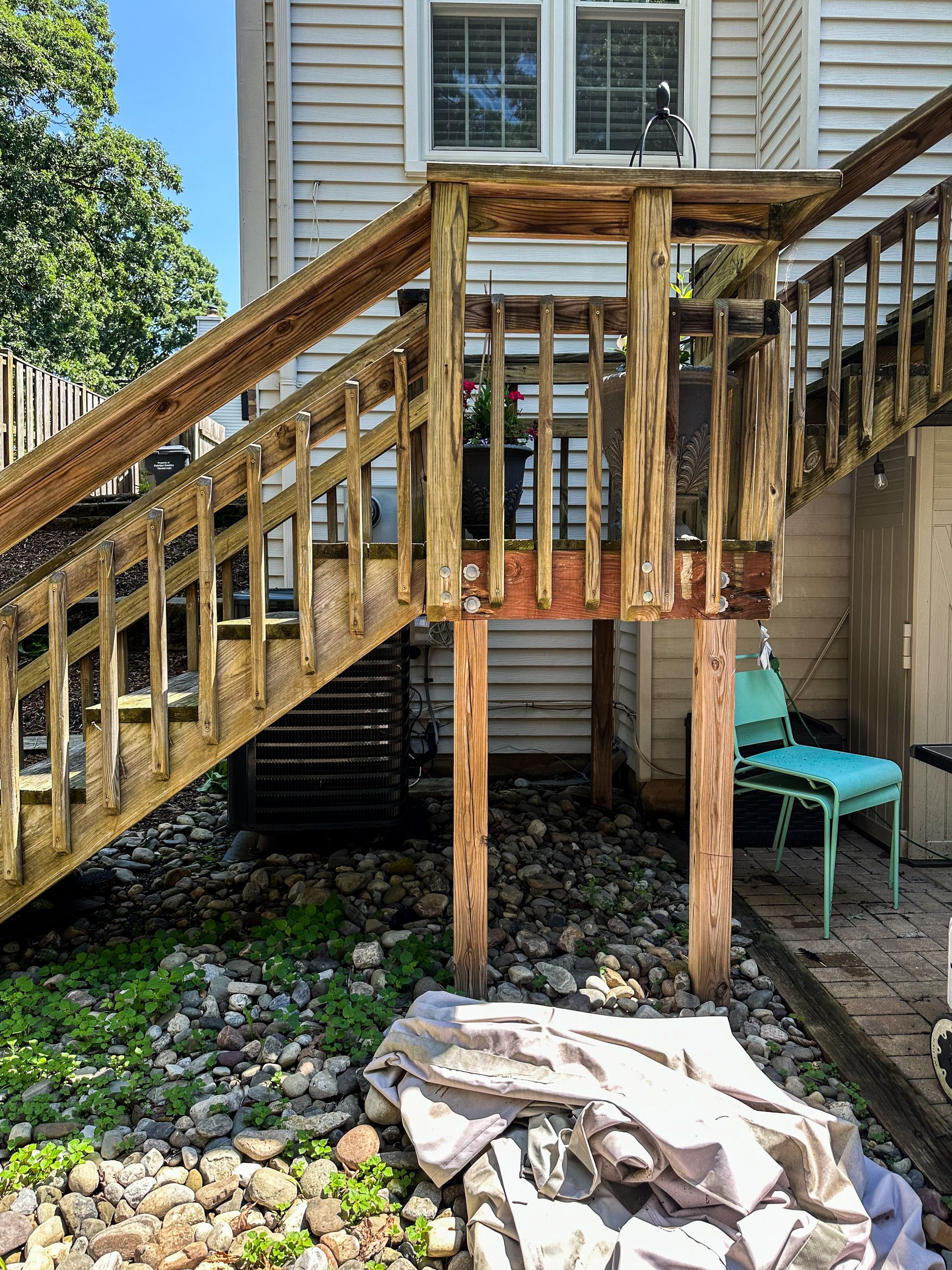 Wooden exterior staircase with weathered wood, leading up to a house. A blue chair sits below the stairs.
