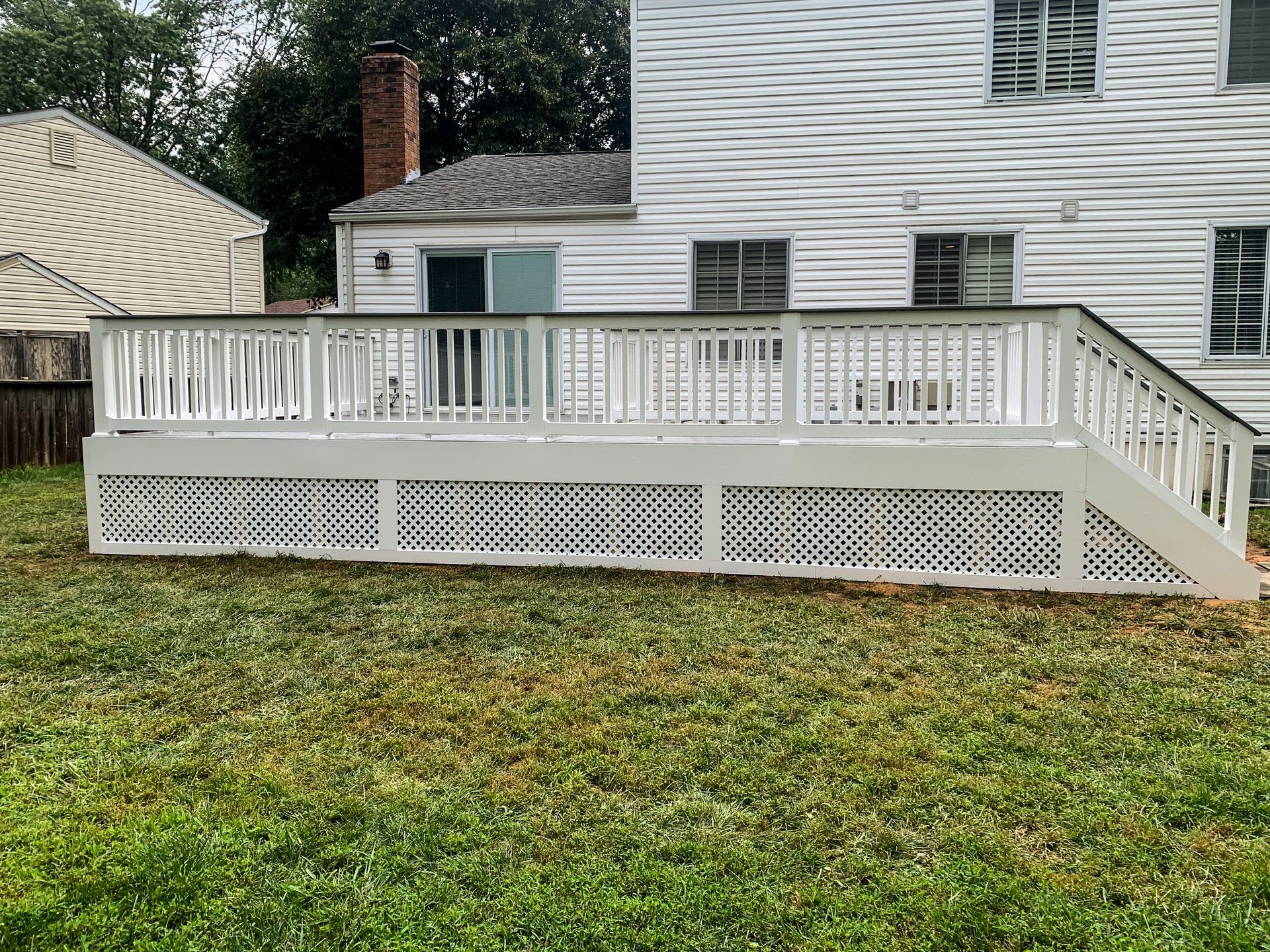 White deck with lattice skirting in backyard, connected to a white house.