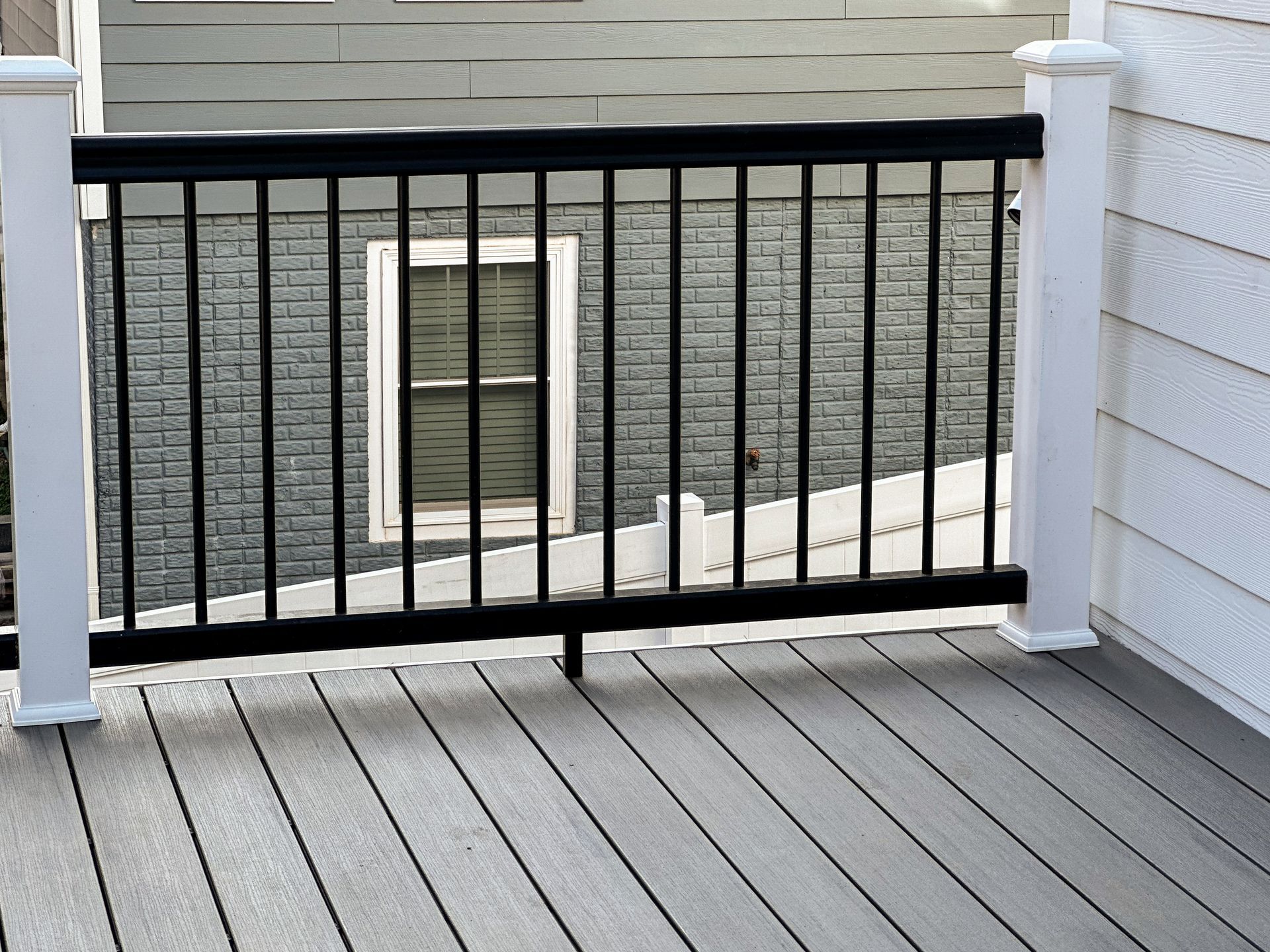 Deck with black railing, white posts, and gray decking, with a building in the background.