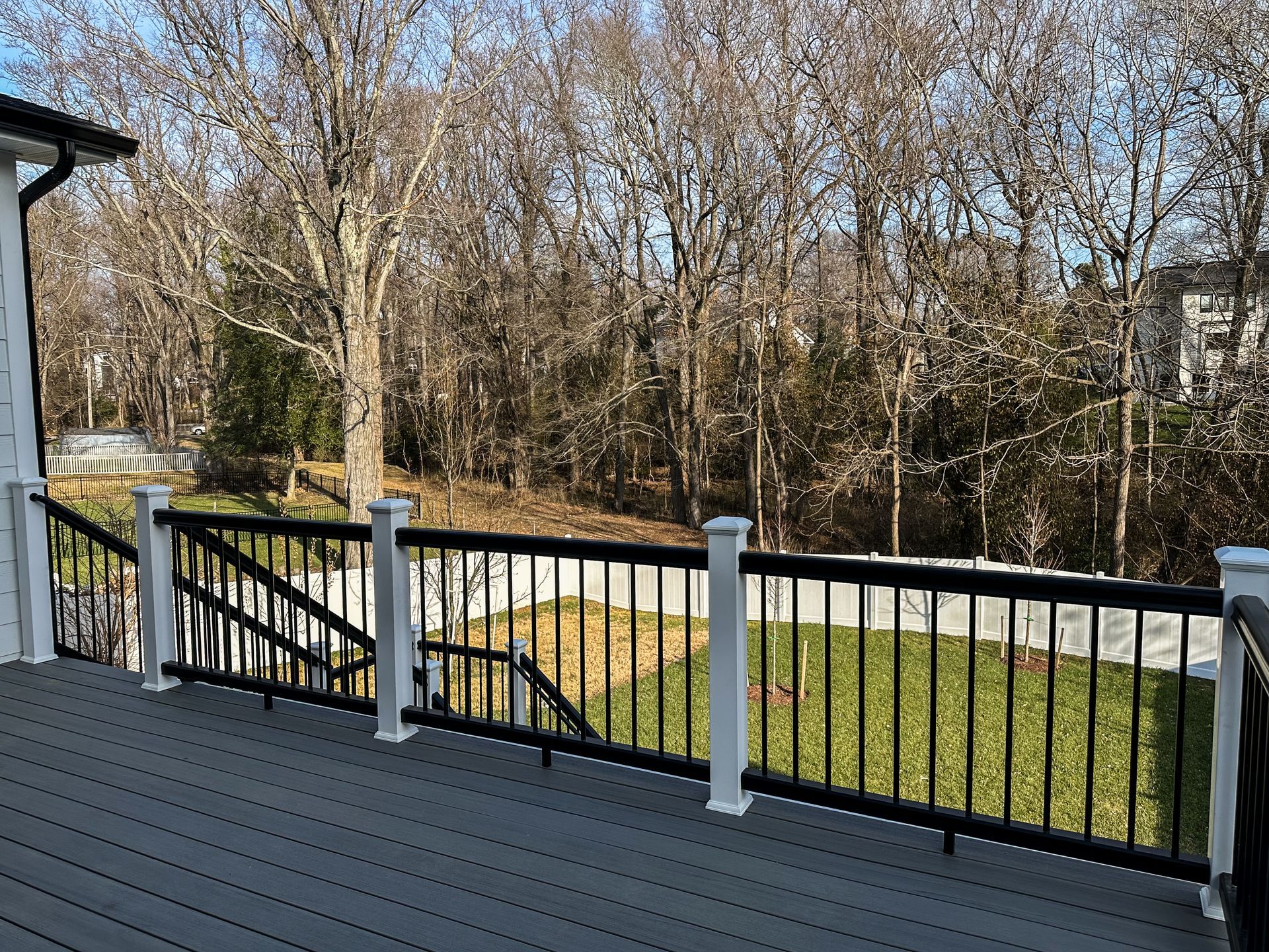 Deck with black railing, white posts, and gray decking overlooking a grassy yard and trees.