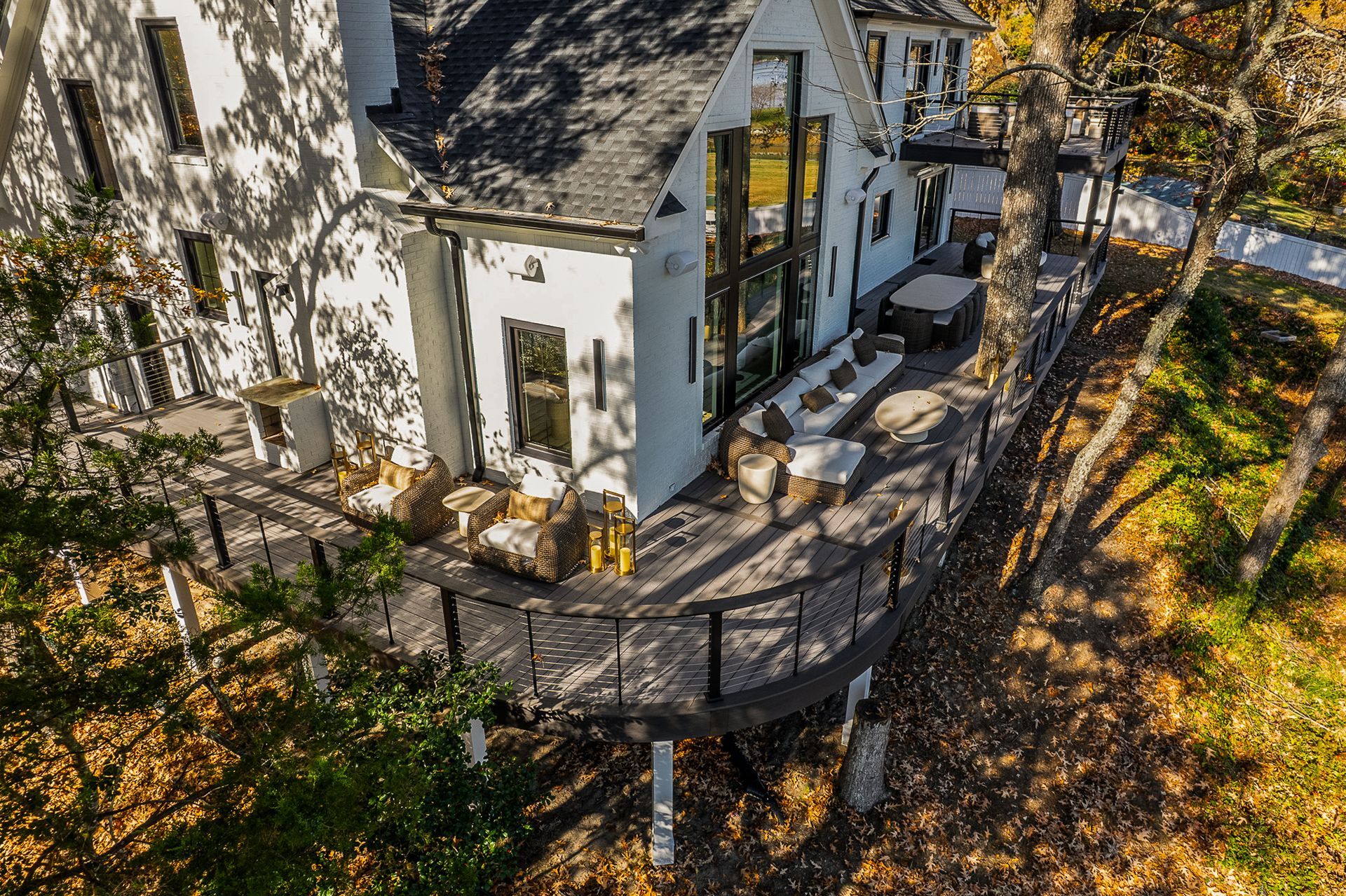 White house with black trim and wraparound deck, set amidst trees with fall foliage.