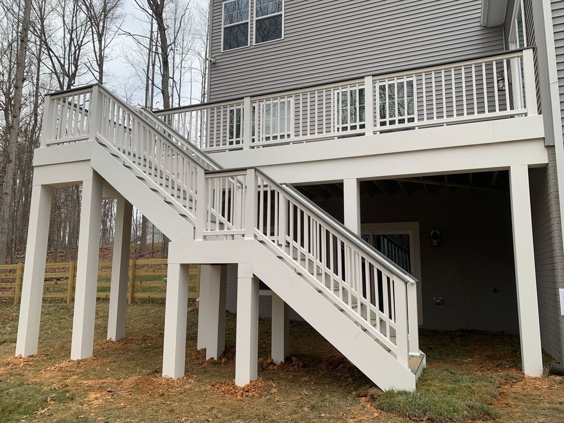 White deck with stairs leading to a two-story home, supported by tall posts.