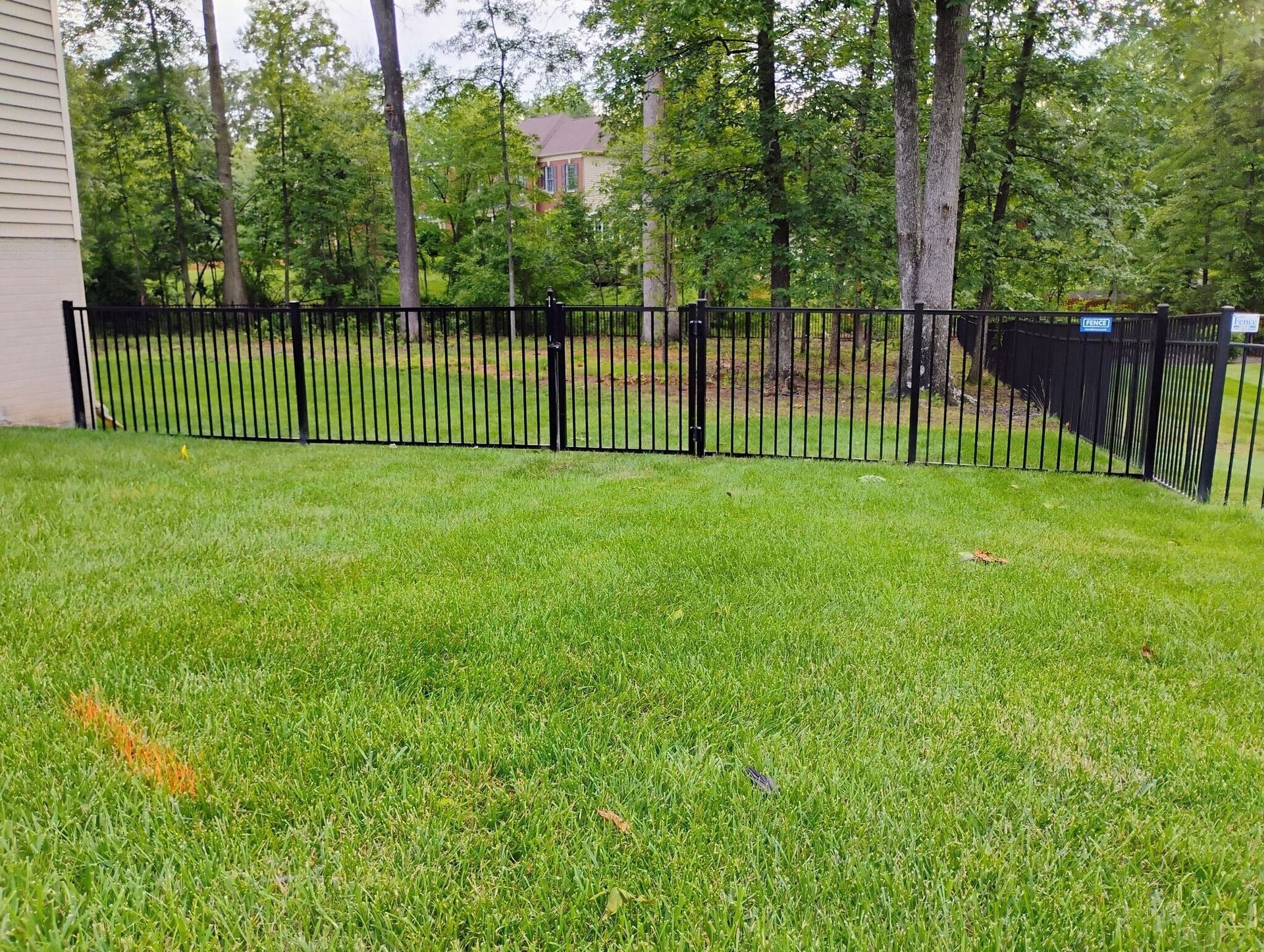 Black metal fence in a green grassy yard with trees in the background.