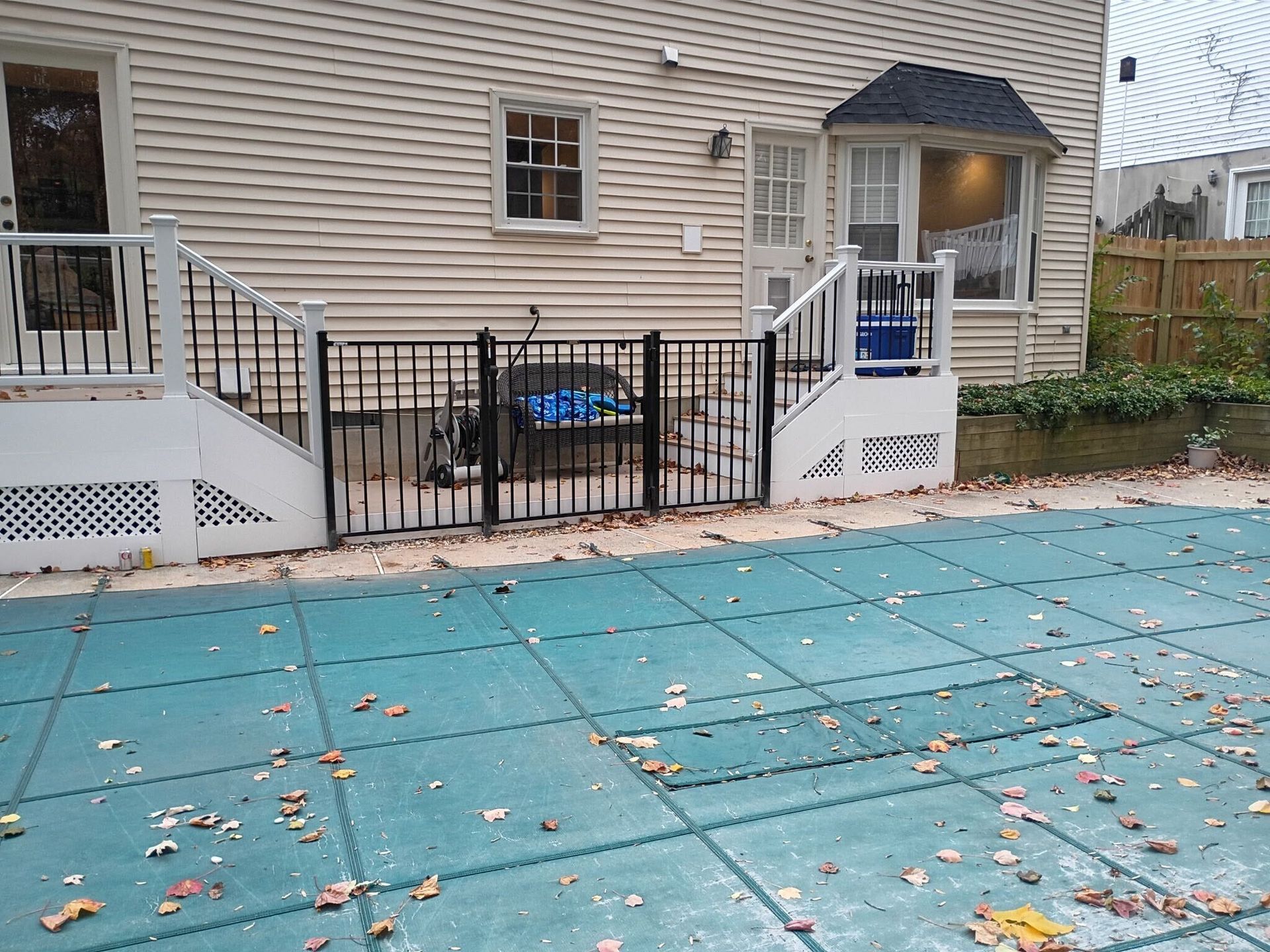 A backyard with a pool covered, a house with a fence and a set of stairs.