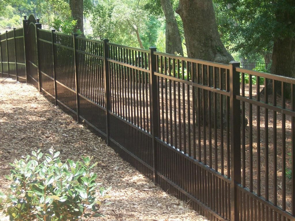 Black metal fence in a yard with trees and mulch.