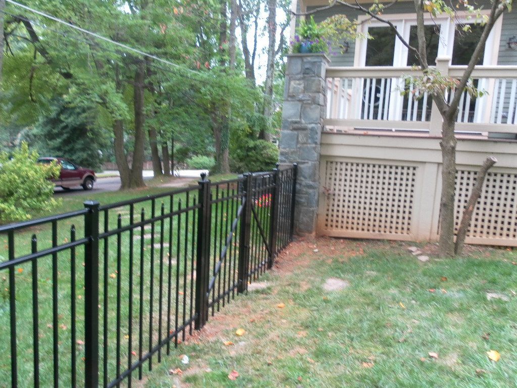 Black metal fence in a yard next to a stone pillar and a house with a white porch.