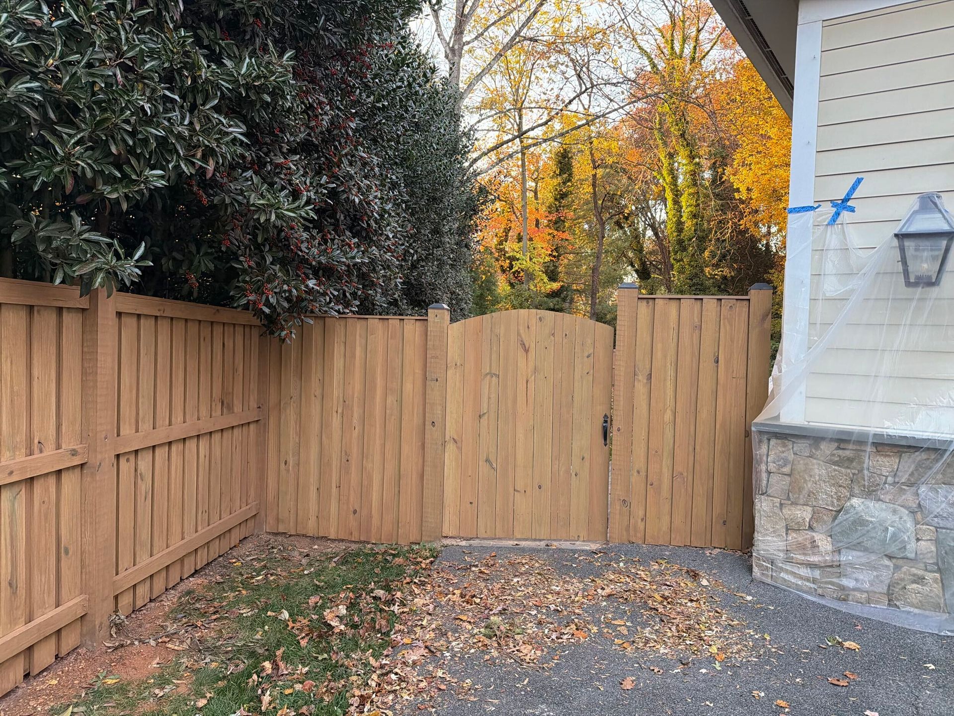 Wooden fence and gate with fallen leaves and colorful trees in the background.