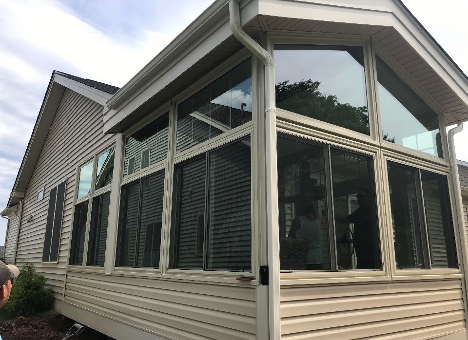 Sunroom addition with large windows, tan siding, and light-colored trim; overcast day.