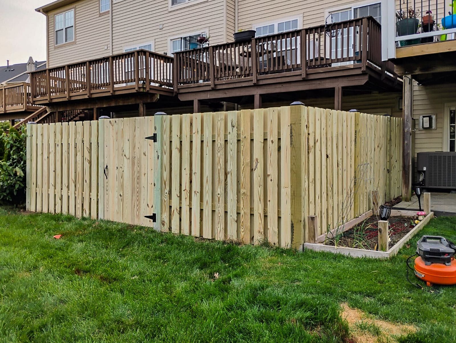 Wooden fence enclosing a backyard with a gate, next to a deck and green lawn.