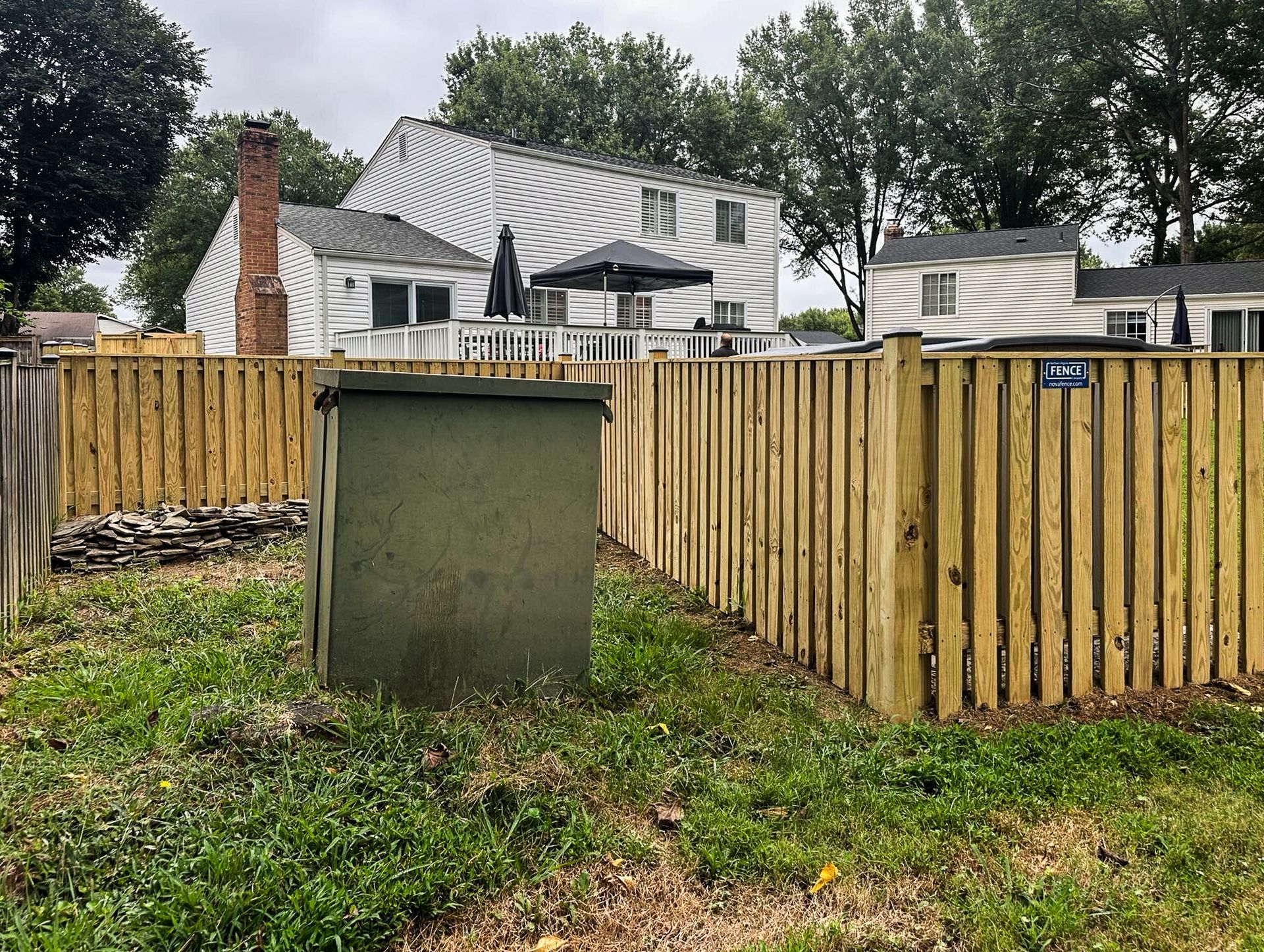 A green utility box within a fenced yard. A house with a striped facade is in the background.