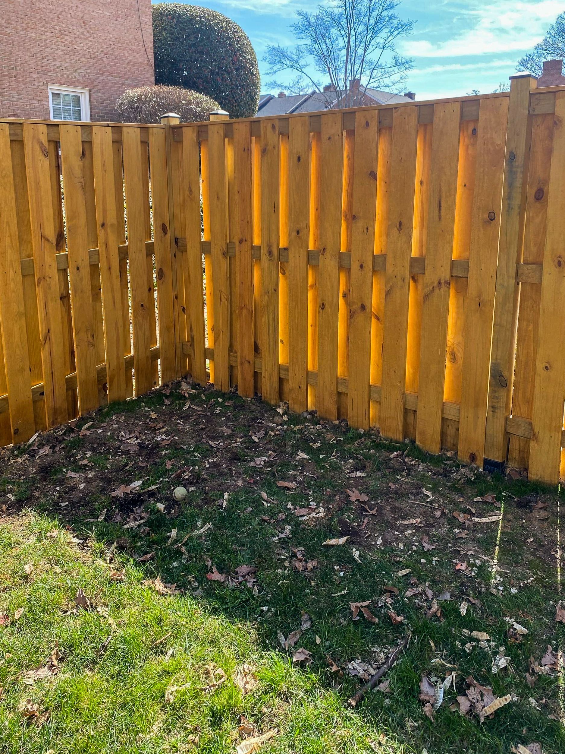 Wooden fence corner with a pile of leaves and grass on a sunny day.