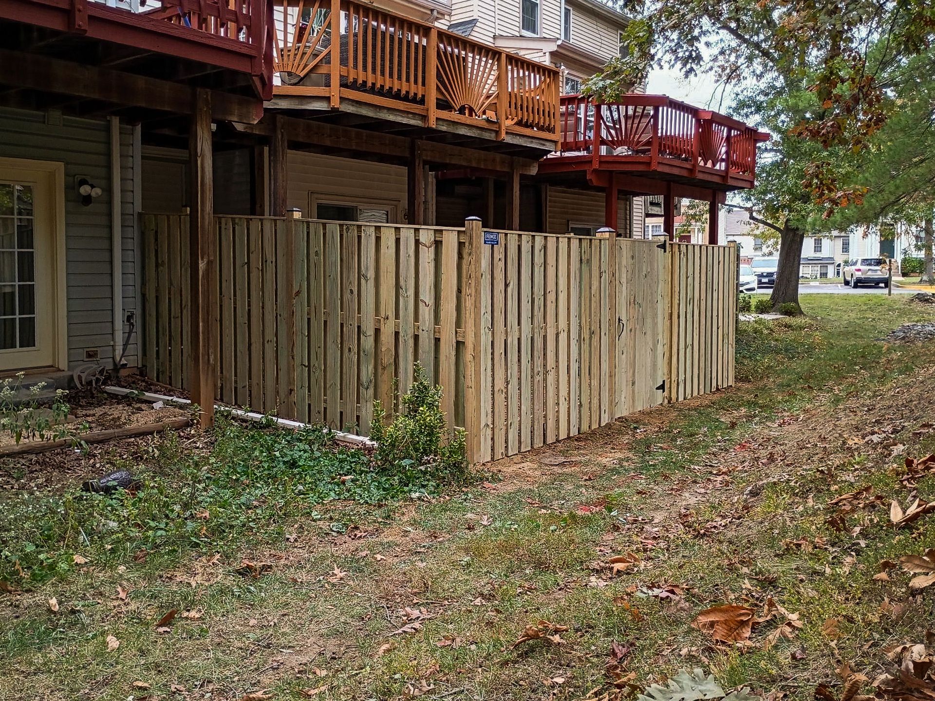 Wooden fence surrounding a patio area under a two-story building with red and brown decks. Overcast sky.