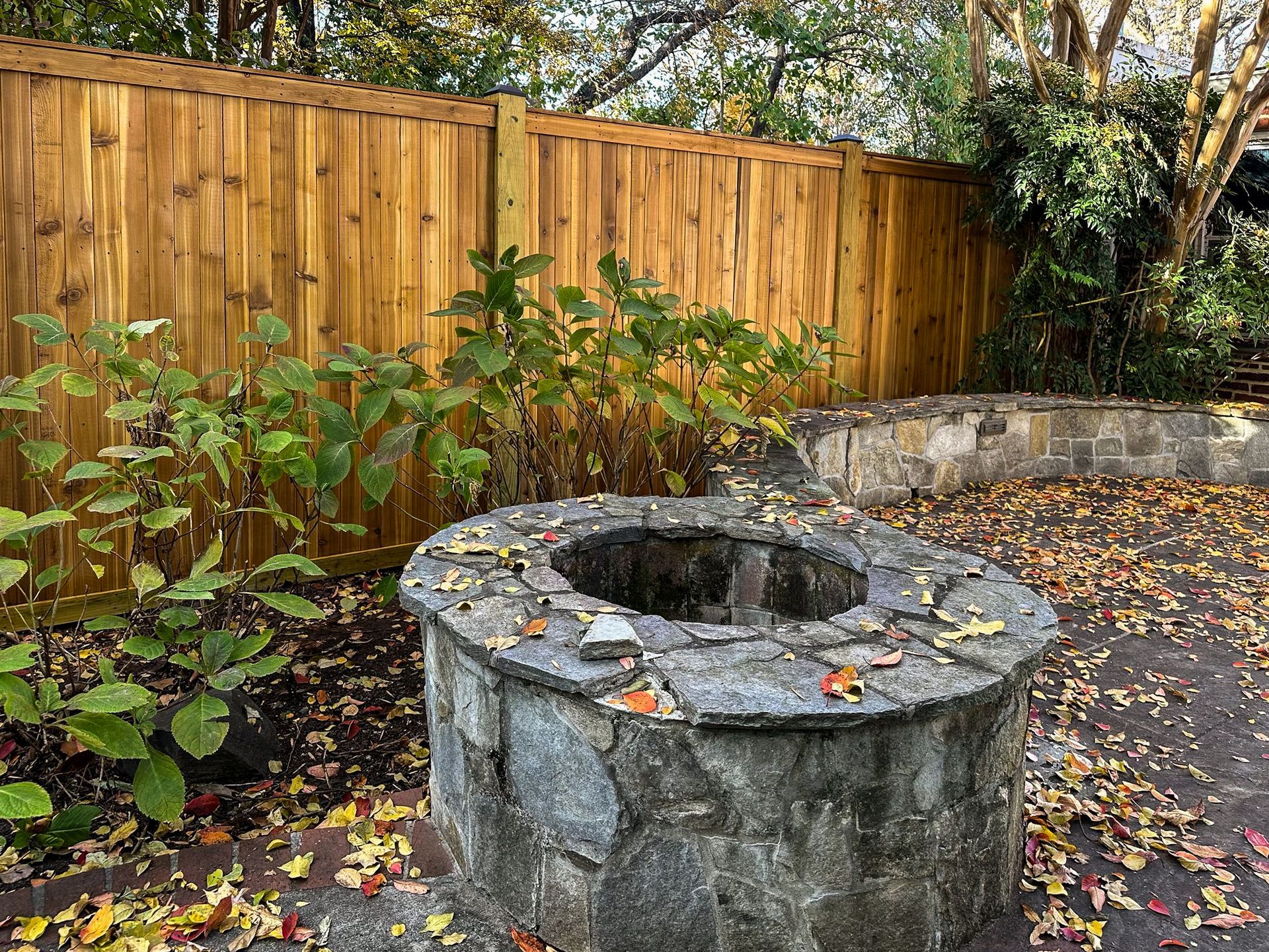 Stone well with wooden fence and foliage in an outdoor setting, covered in fallen leaves.