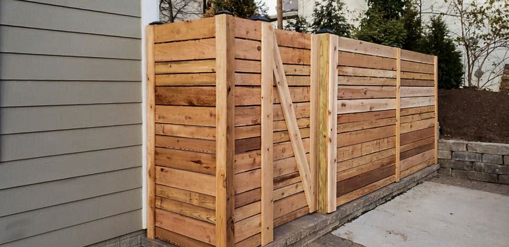 Wooden fence along a building, next to a concrete area.