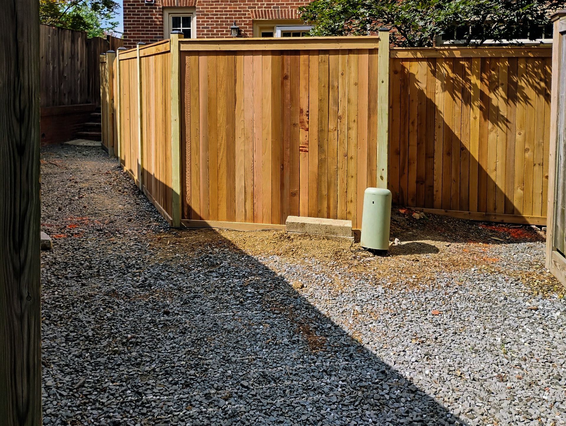 Wooden fence encloses a gravel backyard. A utility box is visible near the fence.