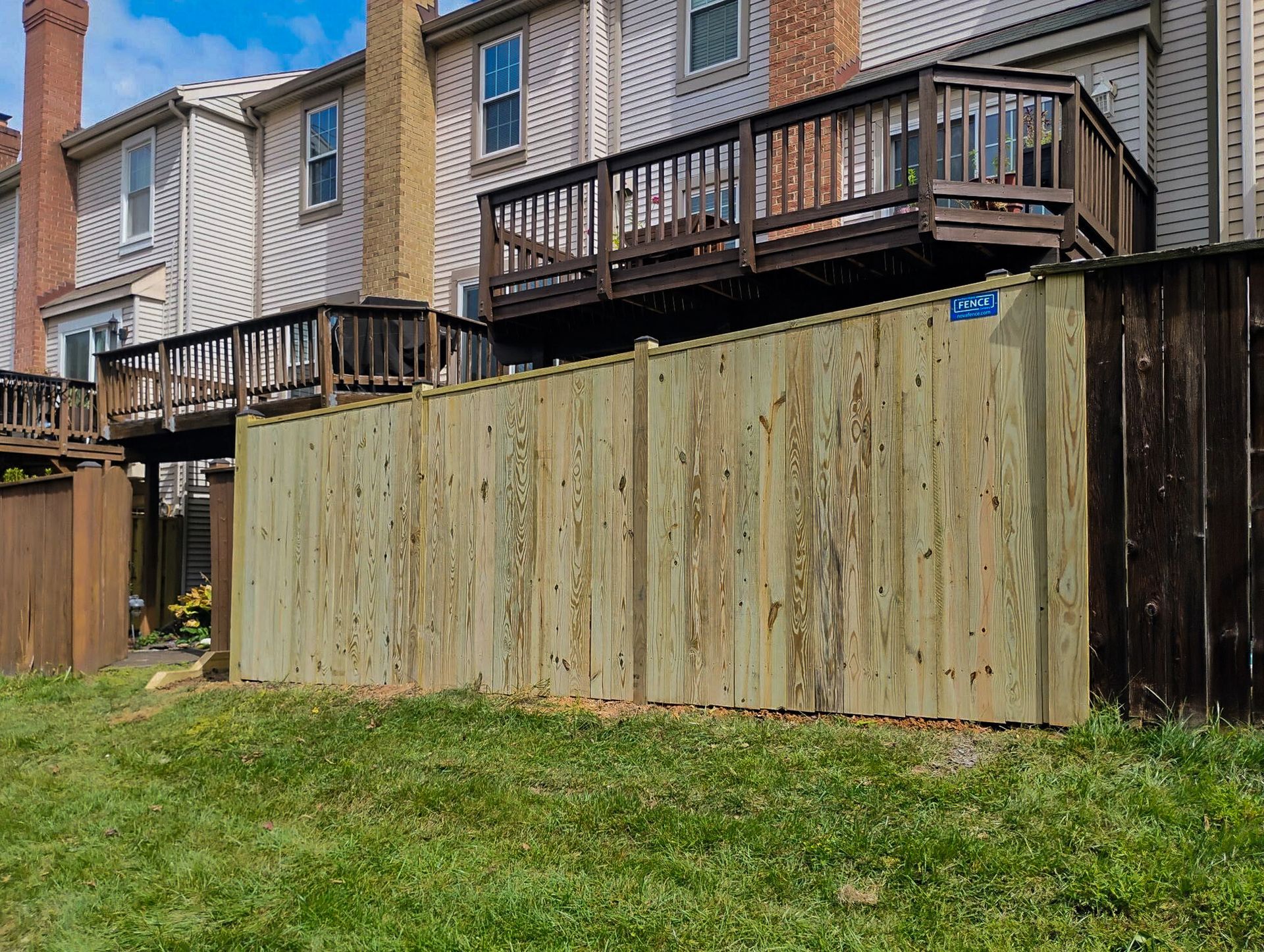 Wooden fence in front of a multi-level deck attached to a light-colored building.