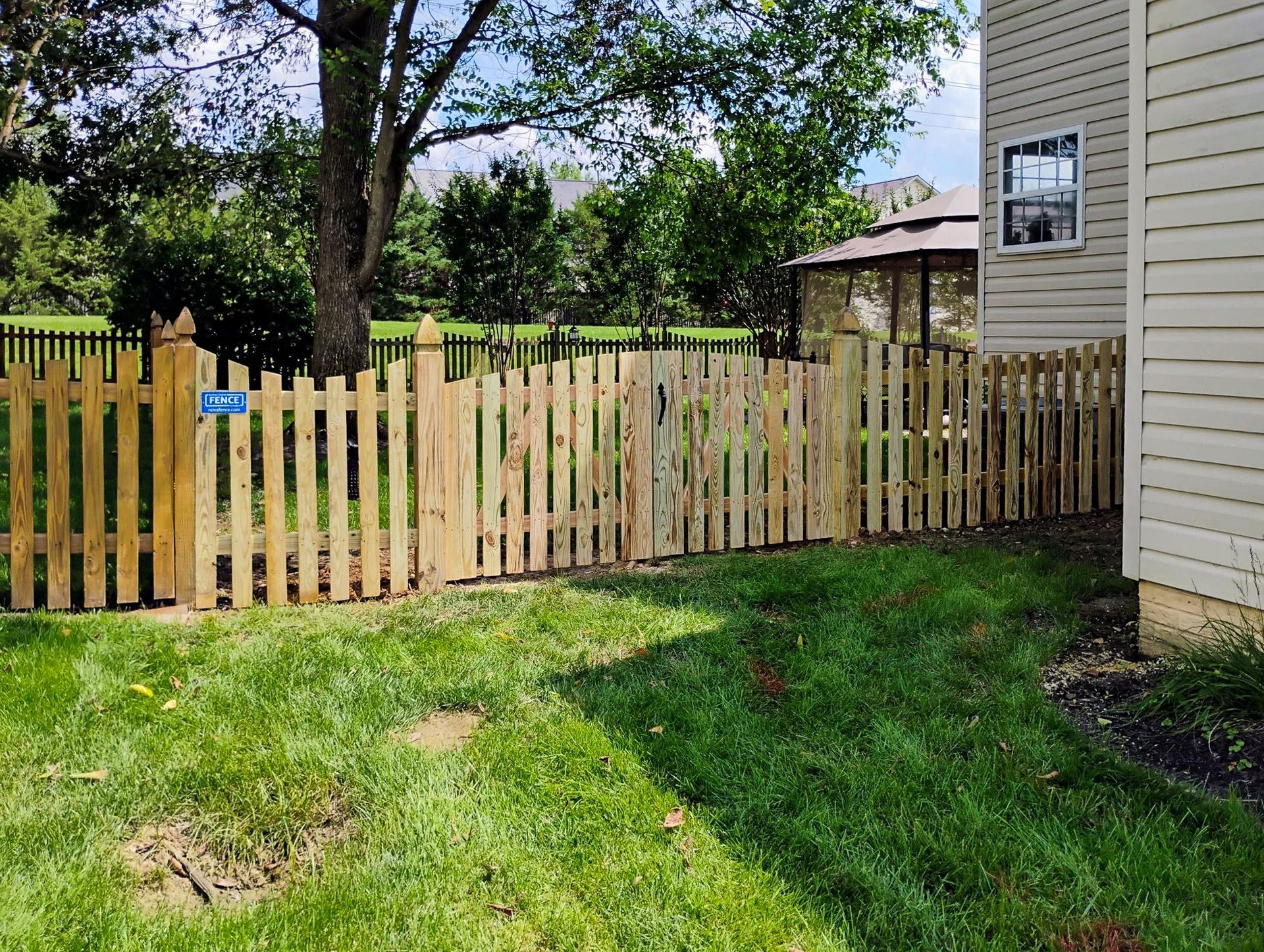 Wooden picket fence in a backyard with green grass, leading to a house.