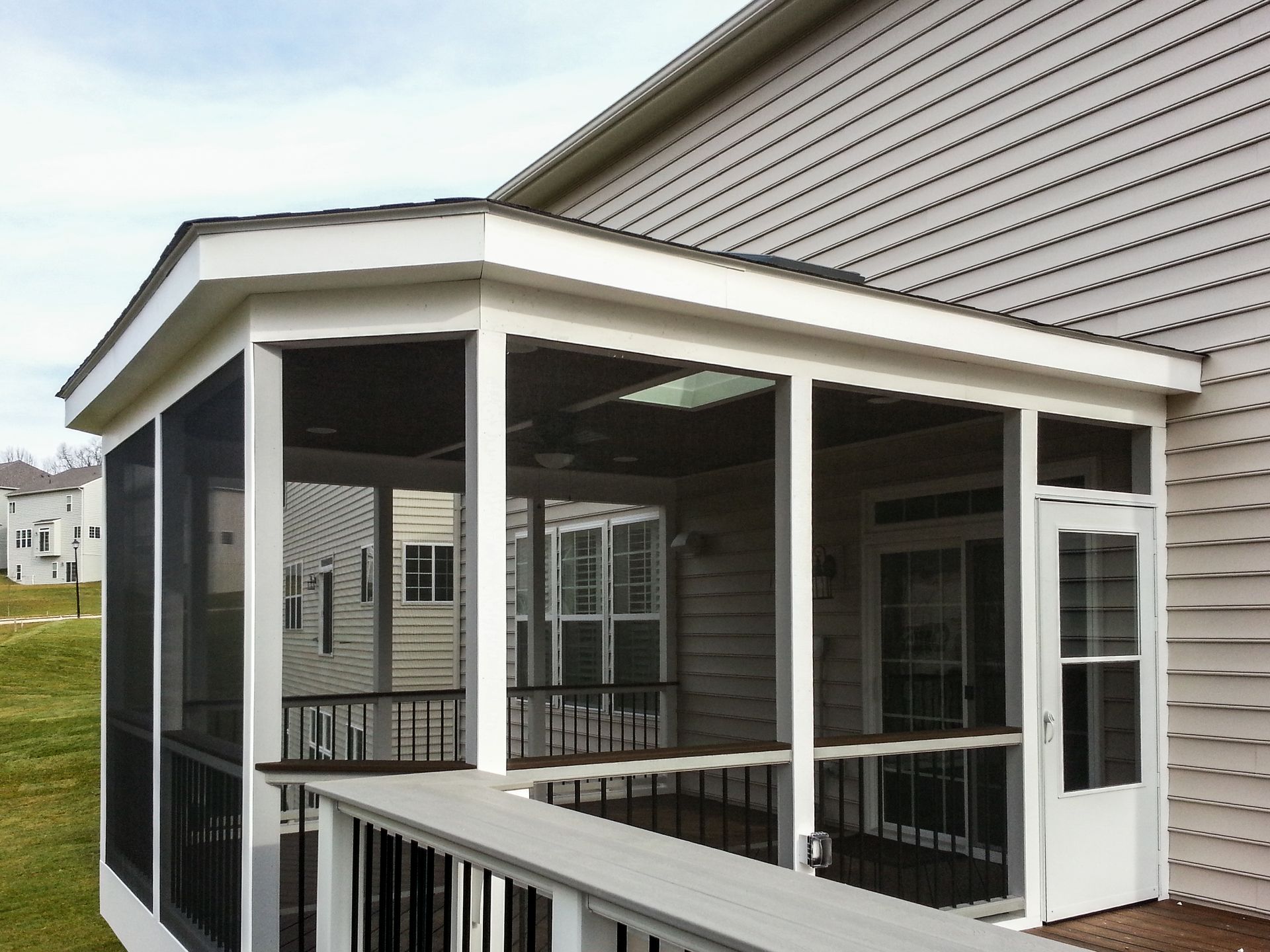 Screened-in porch attached to a house with a white frame, dark screens, and gray deck.