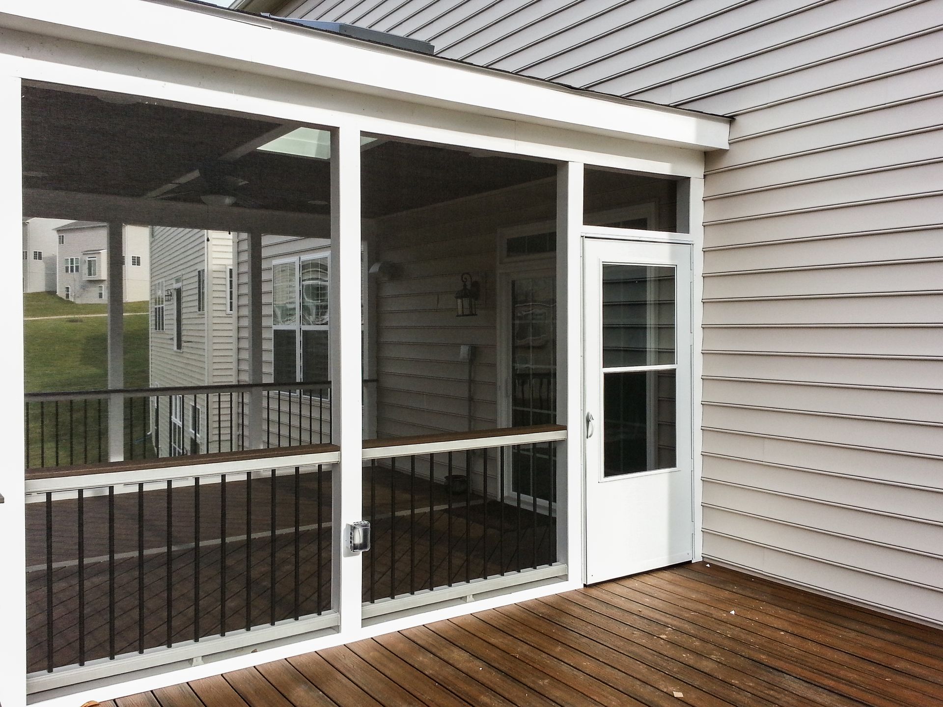 Screened-in porch with wood deck and white siding, white door, and black railing.