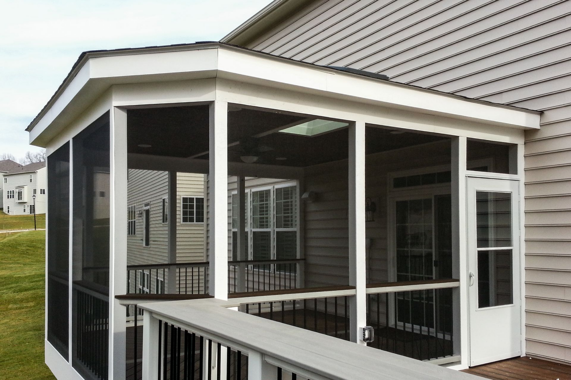 Screened-in porch with white trim, a black railing, and a door, attached to a house with beige siding.