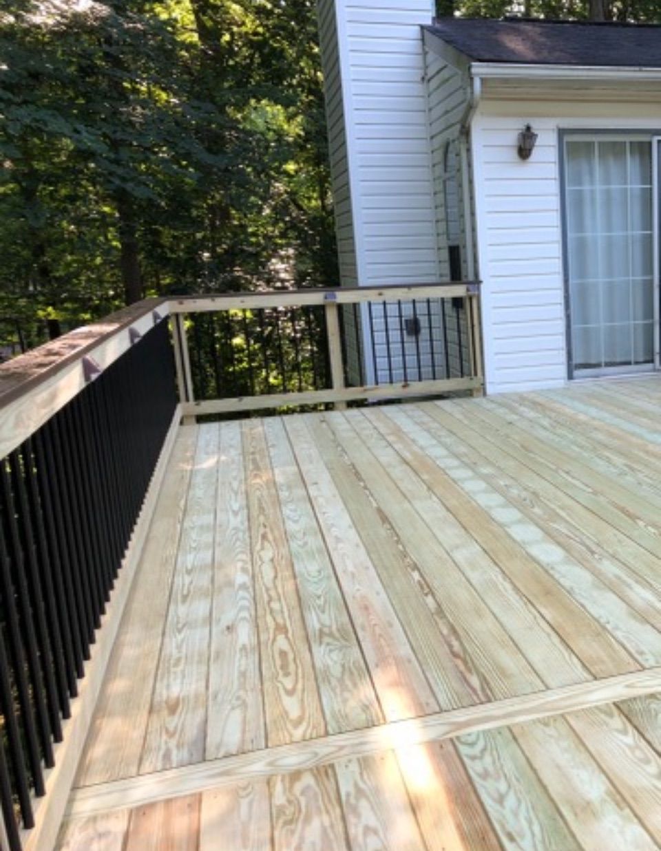 Wooden deck with black railing next to a white house with trees in the background.