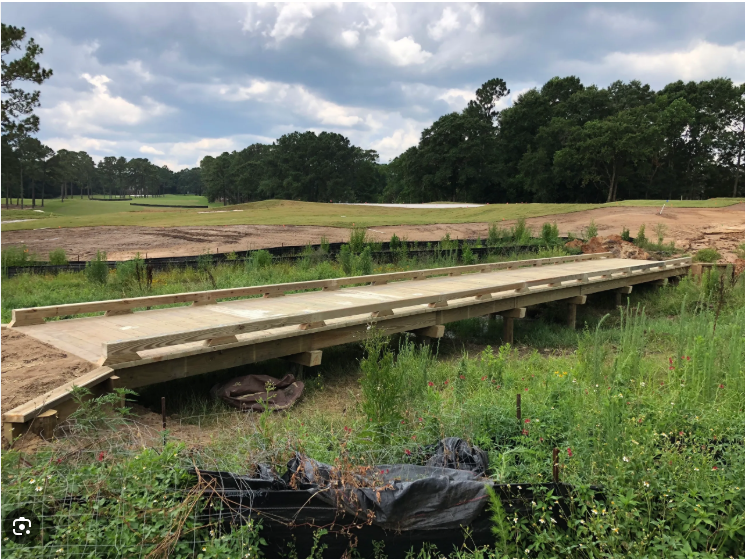 Wooden bridge over a grassy area leading to a golf course.