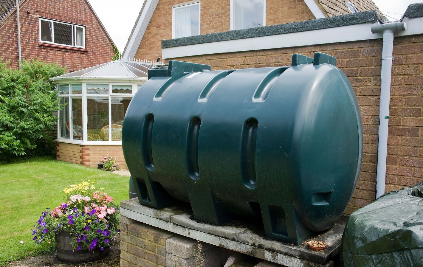 Large green fuel tank on a brick stand beside a house in a garden