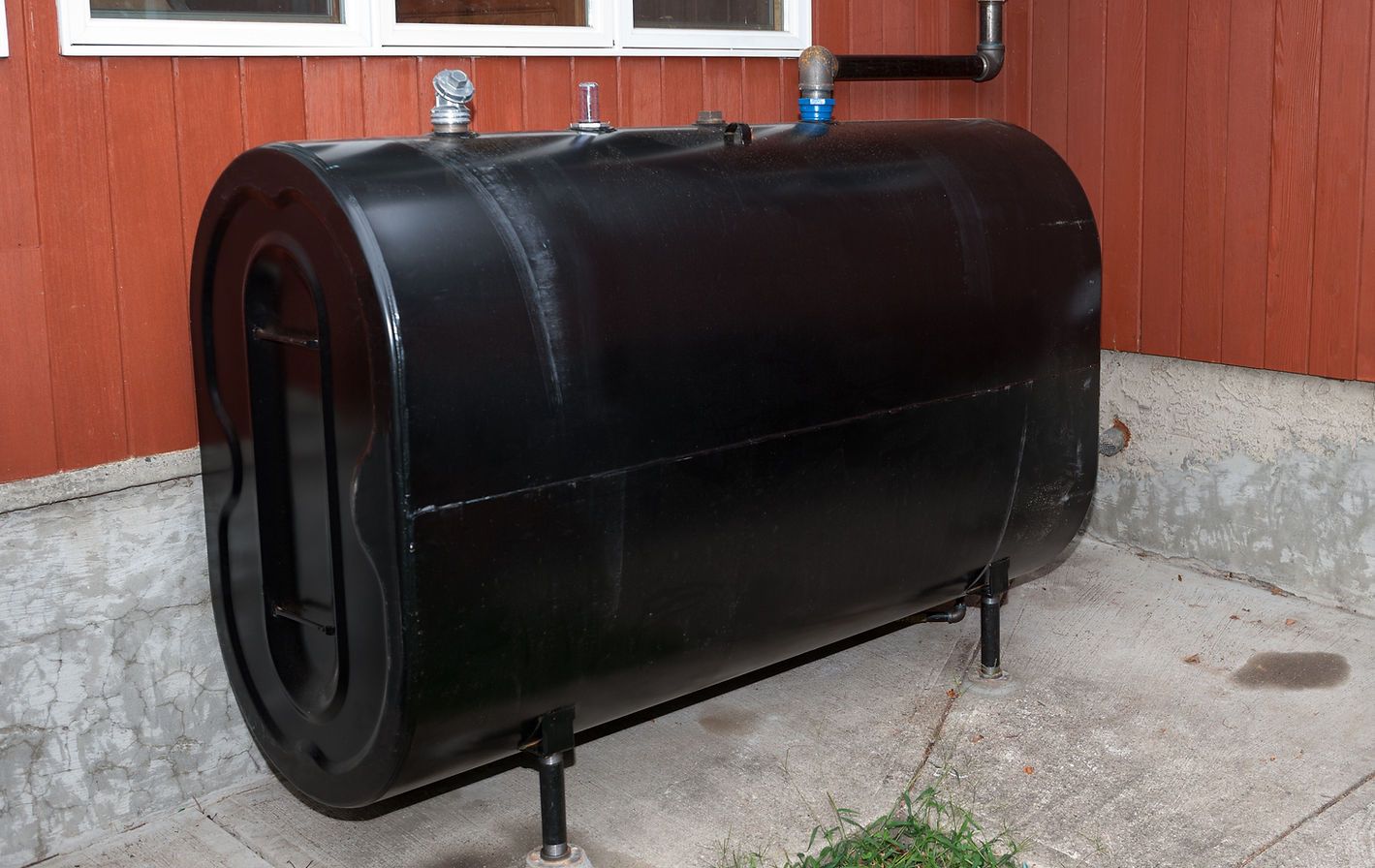 Black cylindrical tank on legs beside a red house wall and concrete foundation