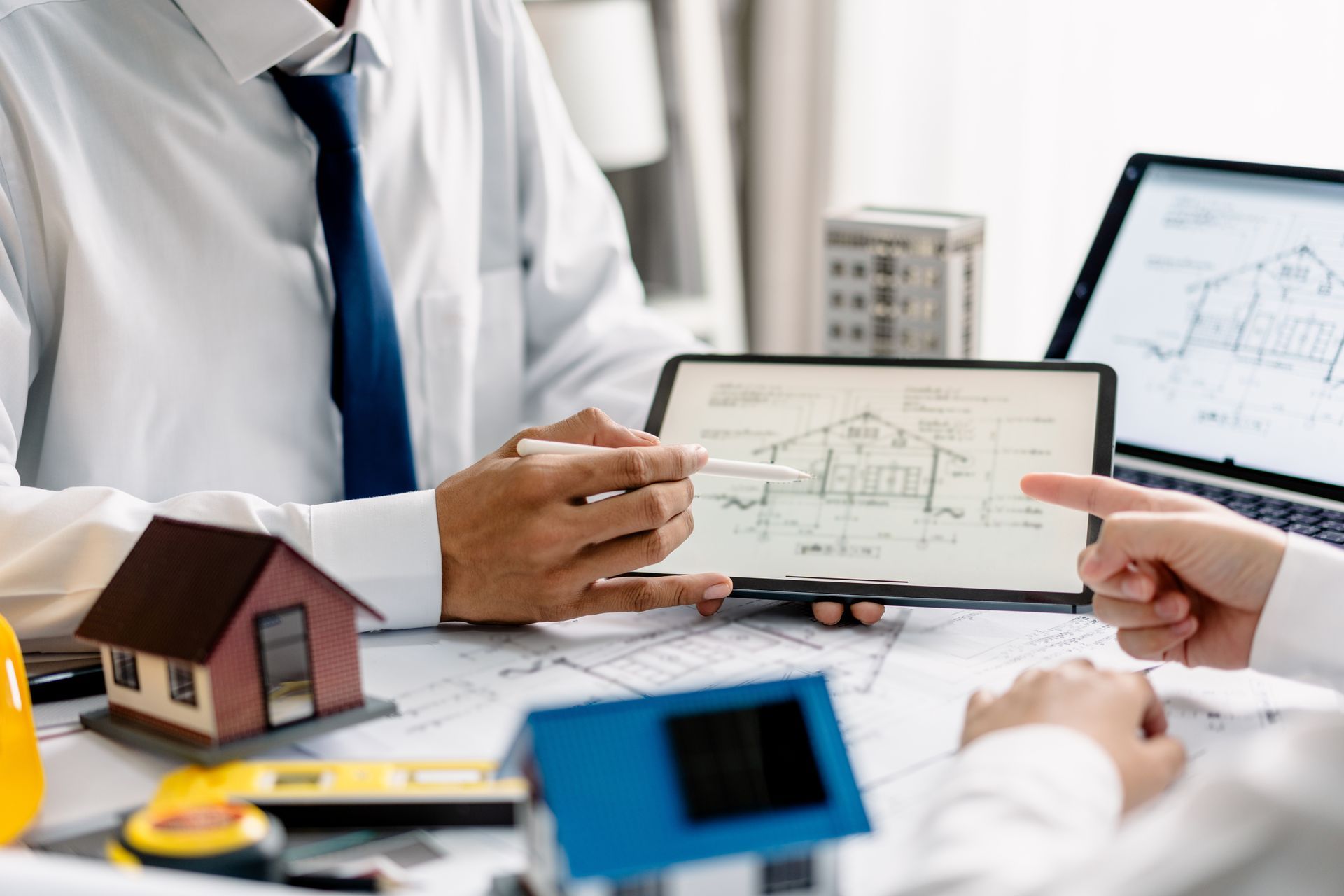 People discussing home insurance at a desk, reviewing property diagrams on a tablet and laptop