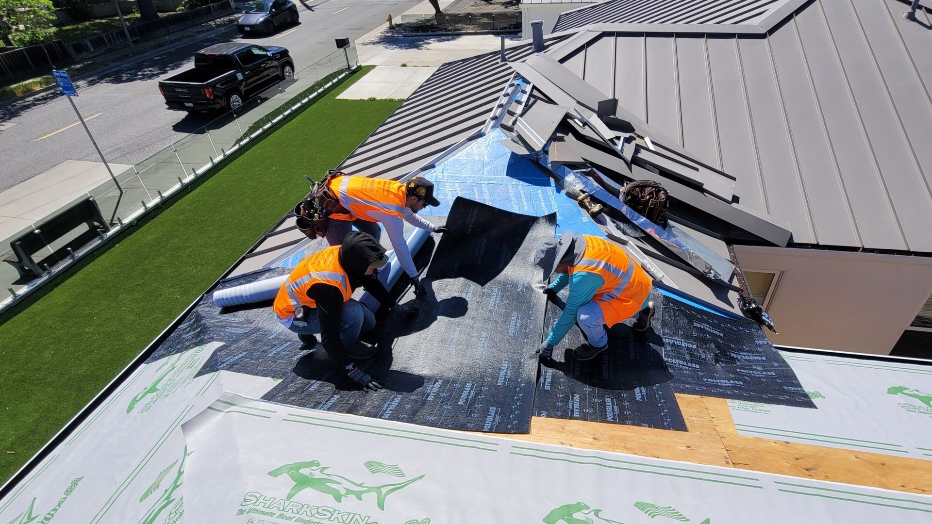 Roofing crew installing shingles on a steep roof with safety harnesses and blue tarp cover