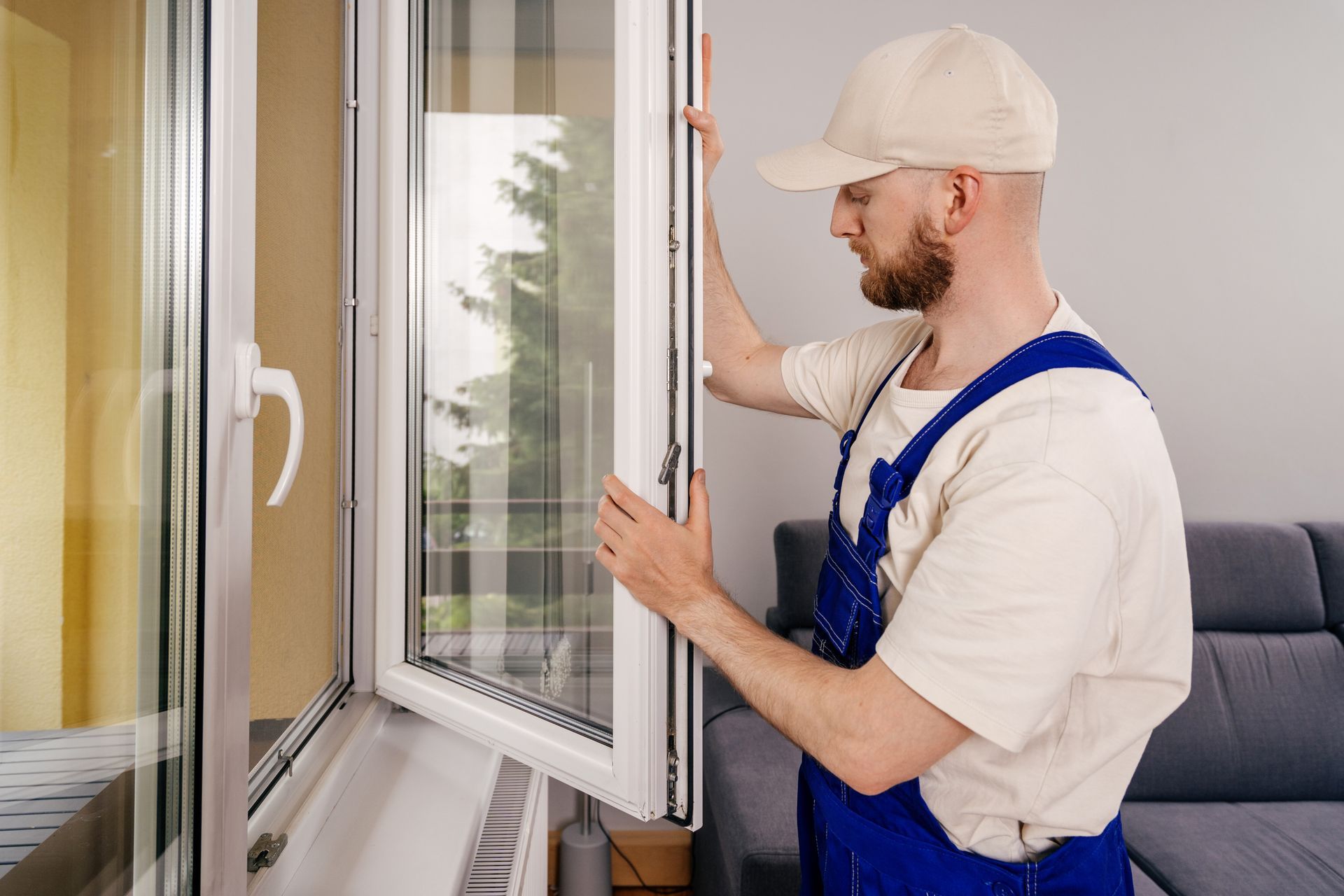 Technician in blue overalls opening a white window indoors