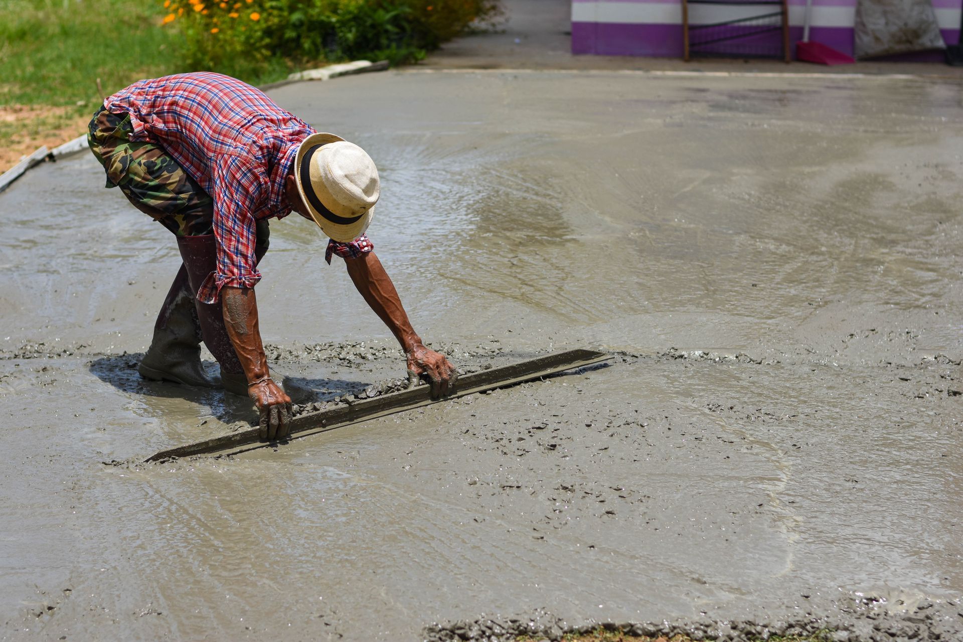Worker smoothing wet concrete with a long tool in an outdoor construction area