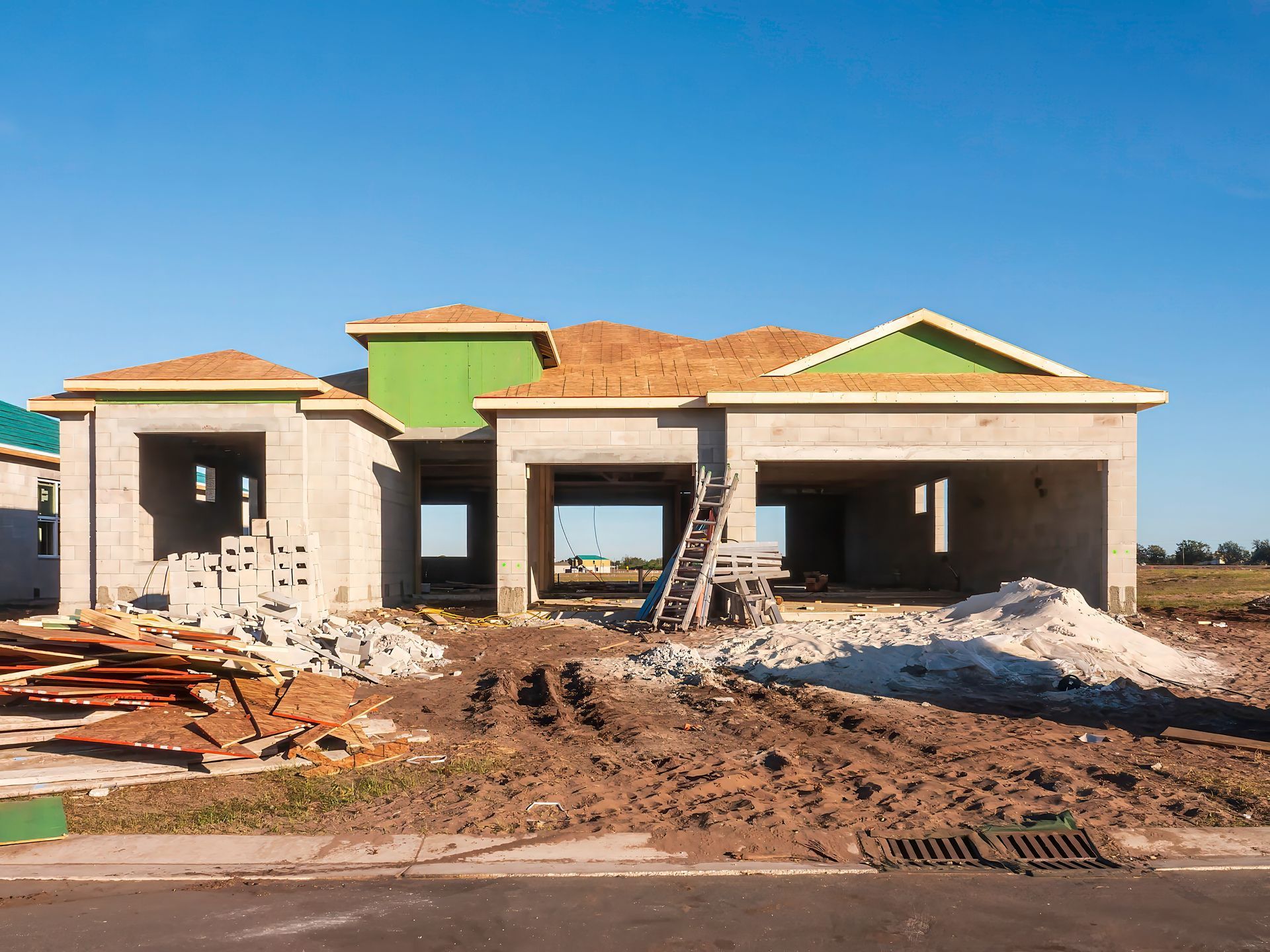 Partially built house with exposed framing, rubble, and dirt in front under a blue sky
