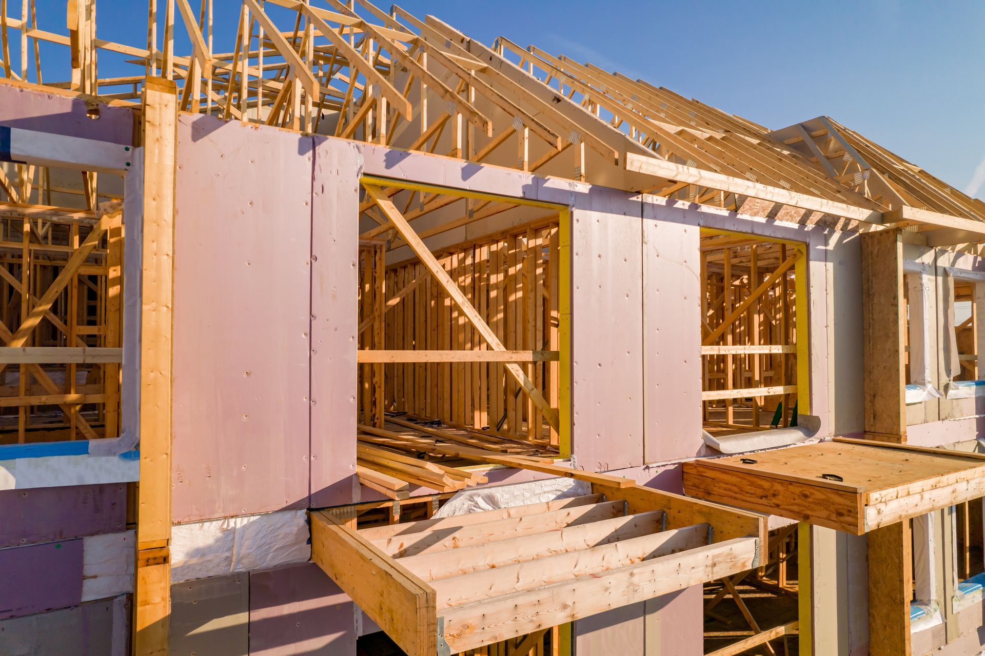 Wood-framed house under construction with pink sheathing and open roof trusses in daylight