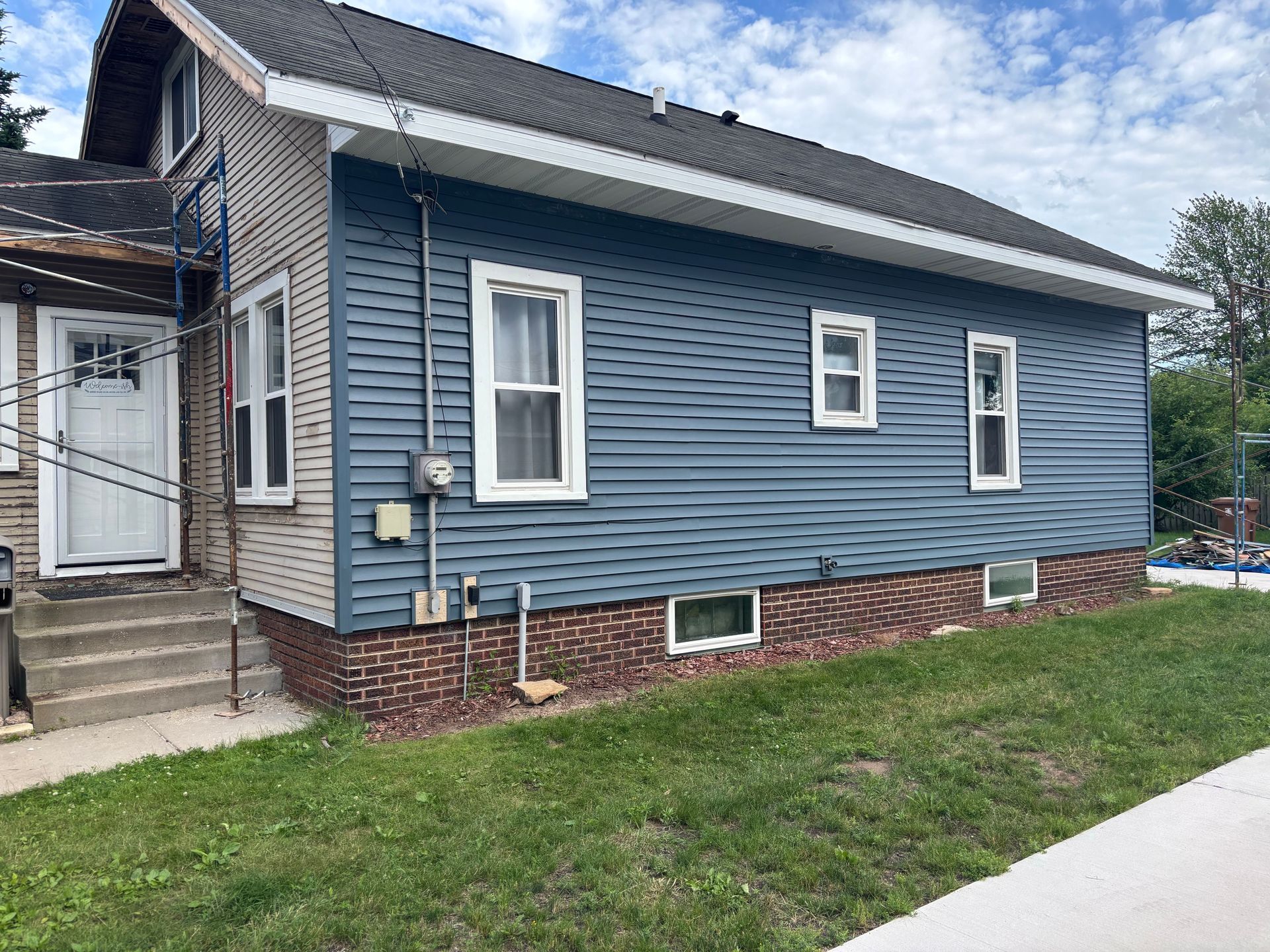 Blue house exterior with white-trimmed windows, brick foundation, and small front steps by a grassy yard