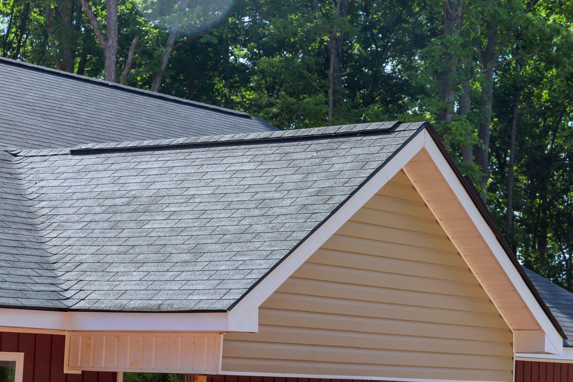 Gray shingled roof and beige house gable against tall green trees