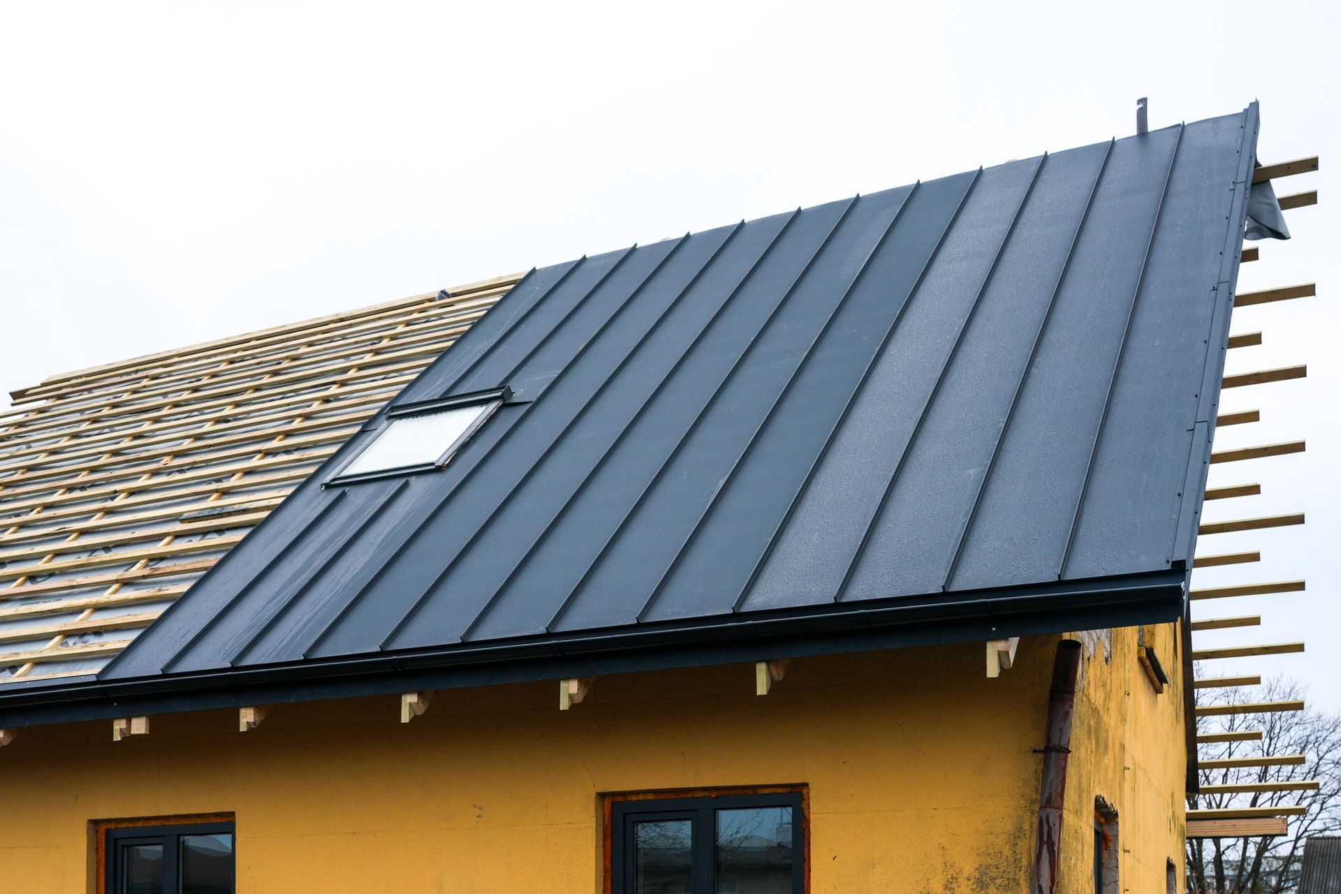 House with dark metal roof under construction, with exposed roof framing and skylight windows