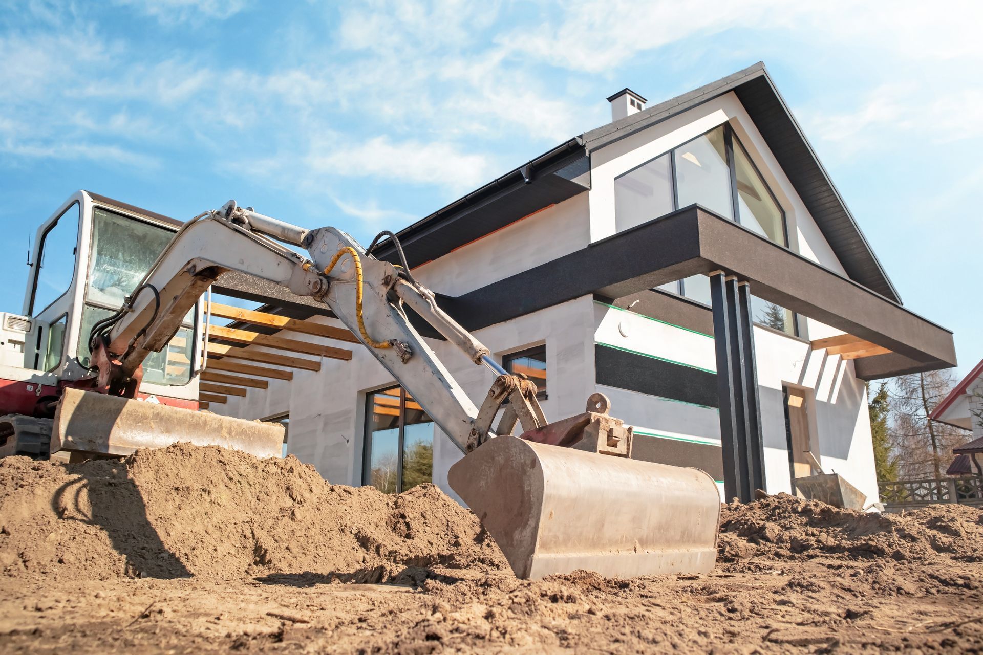 Excavator moving dirt at a house under construction on a sunny day
