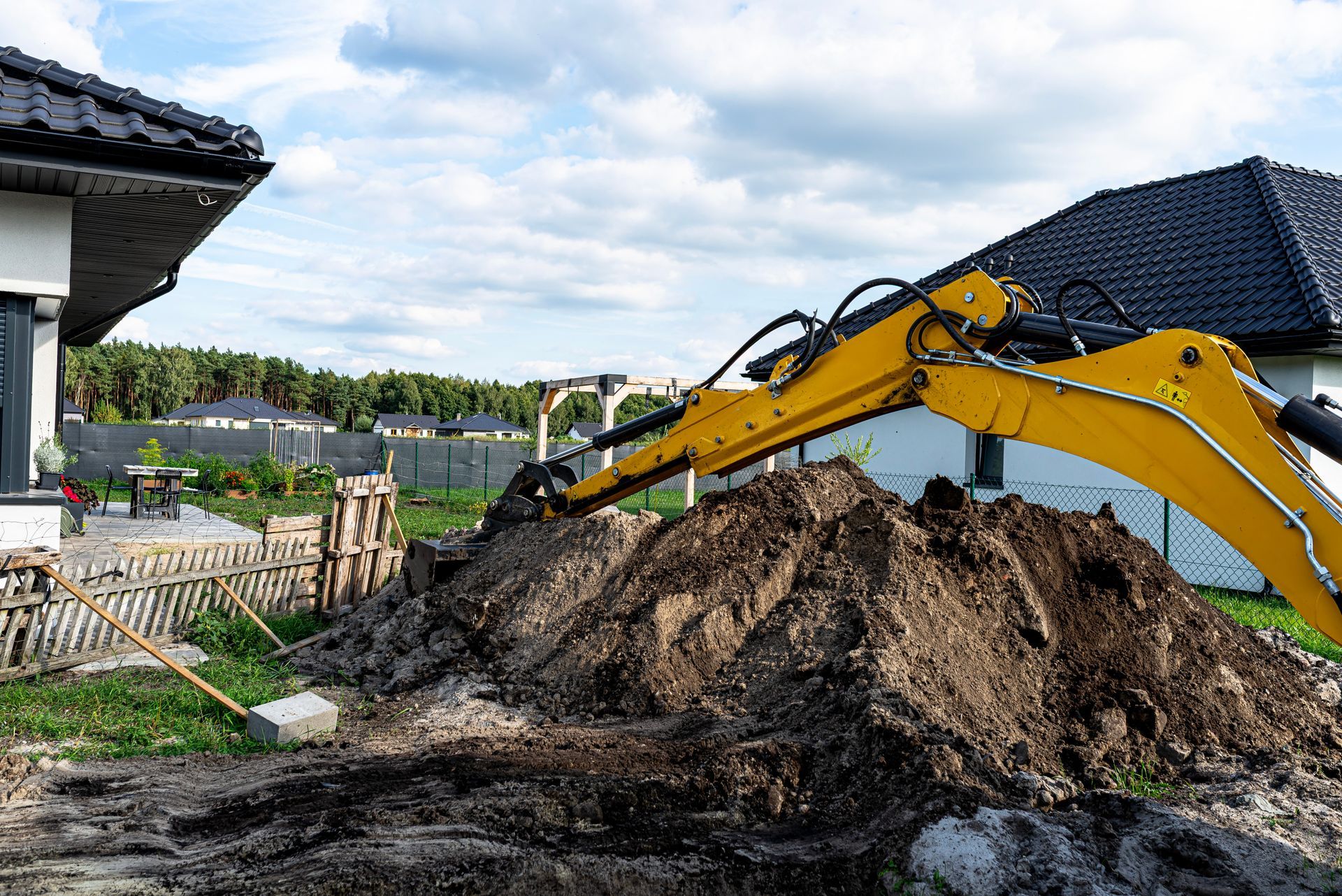 Yellow excavator digging a dirt pile beside a house in a residential yard