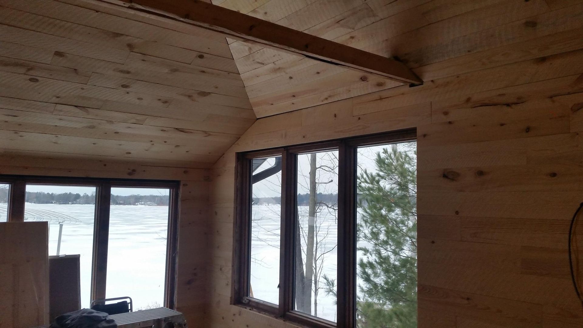 Interior of wooden cabin with windows overlooking a snow-covered lake.