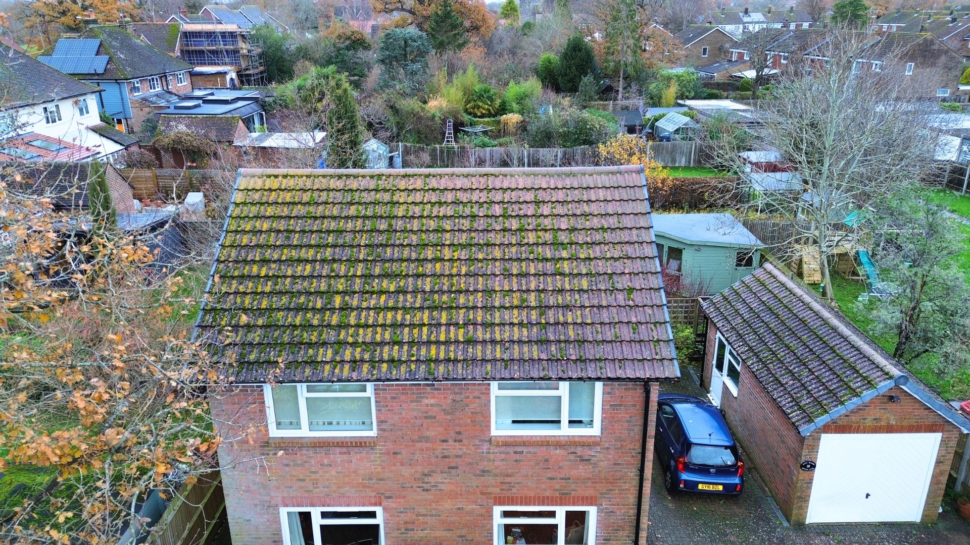 Overhead view of a two-story brick house with a mossy roof and a detached garage, car parked in the driveway.