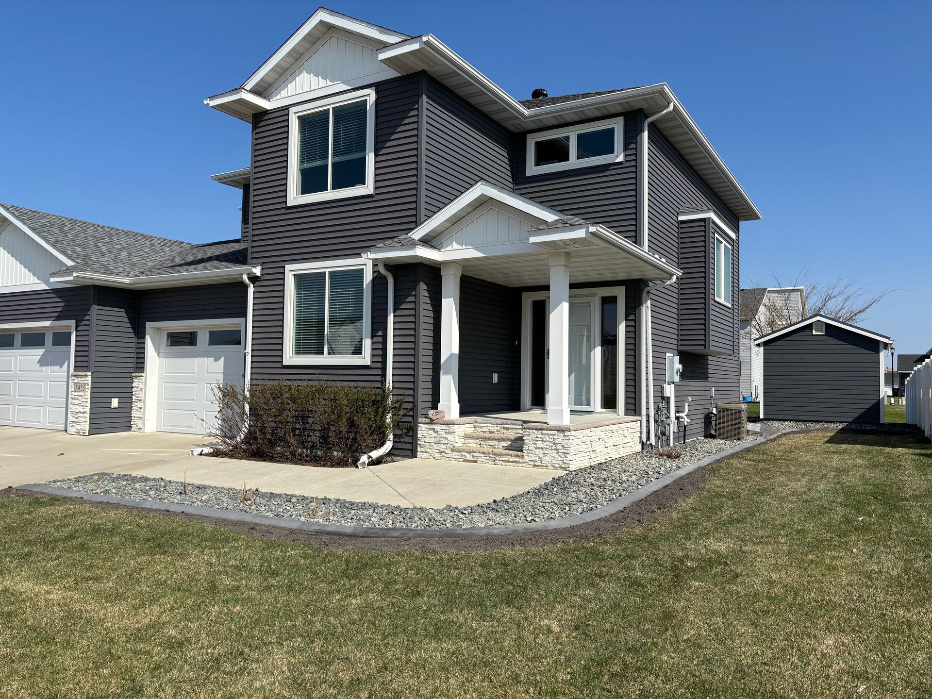 A two-story house with dark gray horizontal siding, white trim, a covered front porch, and a small detached shed.